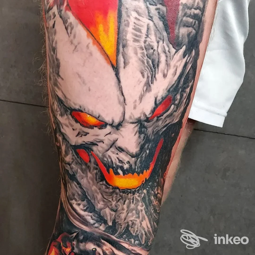 Tatuaggio reale su pelle della gamba raffigurante una creatura minacciosa con colori arancione e rosso, realizzato dallo studio The Ink Man a Villa San Giovanni.