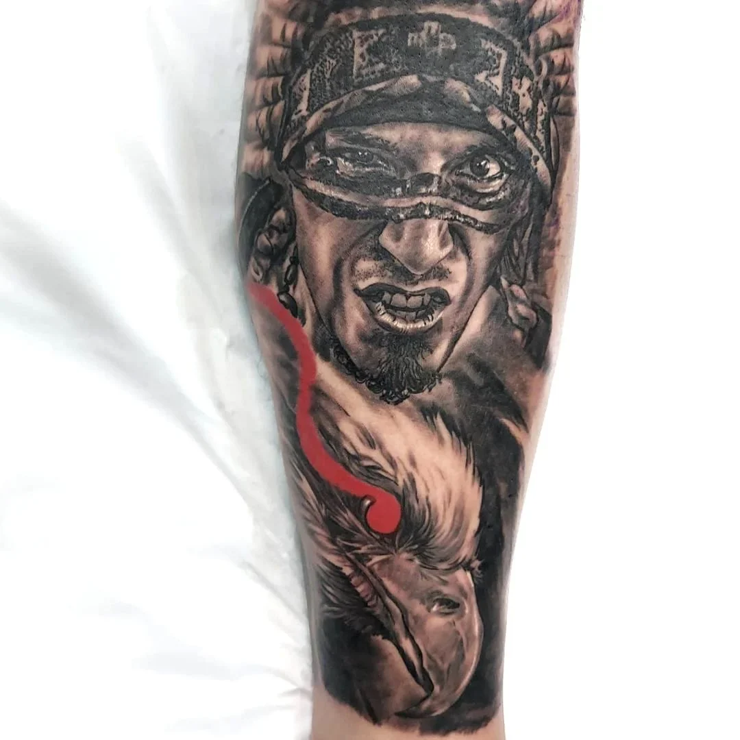 Tattoo realistico sull'avambraccio raffigurante un volto con maschera e una testa di cervo in tonalità nere e grigio, tratto con dettagli precisi e ombreggiature profonde.