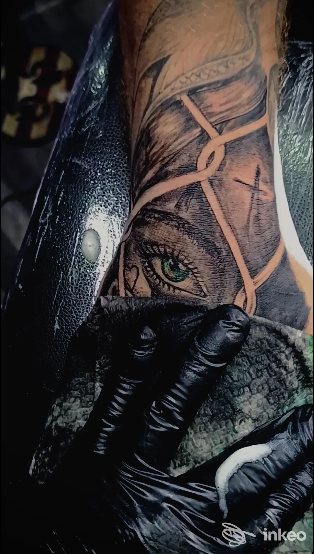 Dettaglio di un tatuaggio su pelle presso Black J Tattoo a Tortora: un occhio verde incorniciato da linee geometriche e una mano nera guantata.