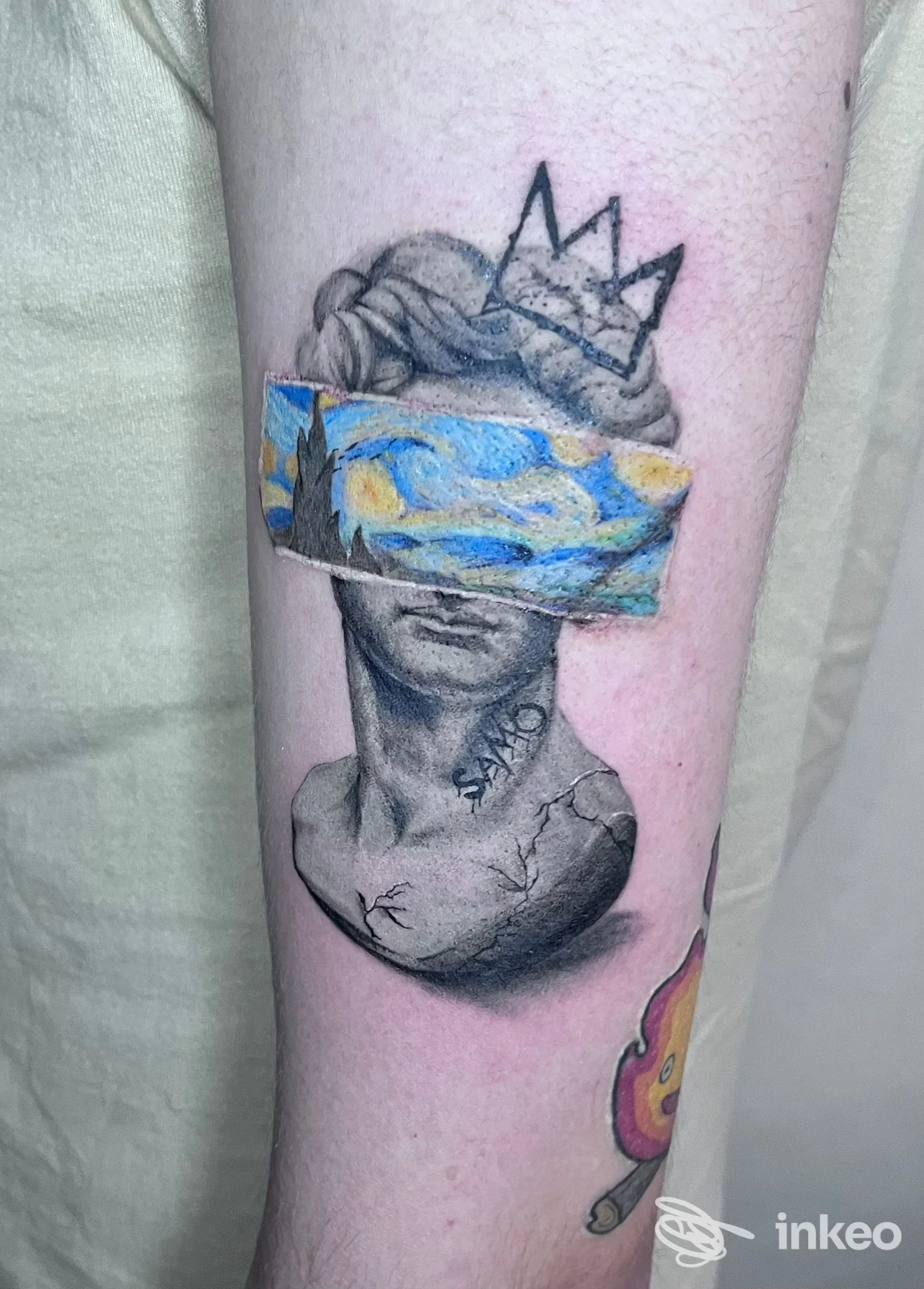 Tatuaggio corporeo su avambraccio raffigurante busto di statua con corona, con una cornice colorata che mostra paesaggio; realizzato presso Studio Ugo DMB Tattoo a Quattromiglia, Italia.