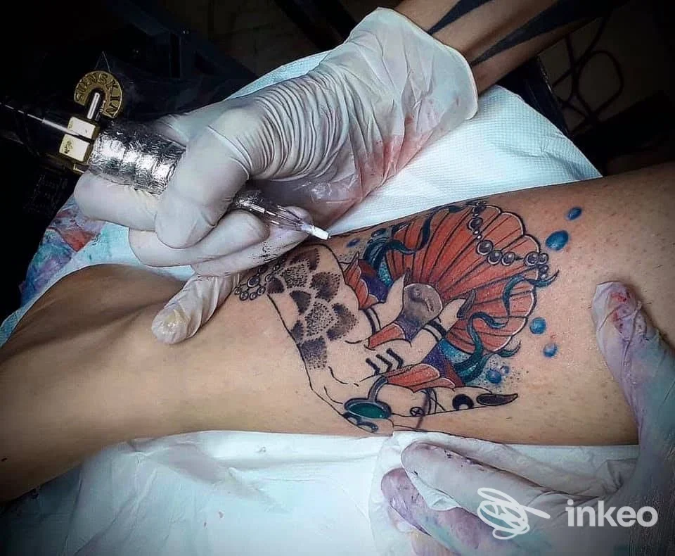 Tatuaggio in corso su pelle di una gamba a Cosenza nello studio LAle.tattoo, con operatore guantato che lavora sul disegno colorato.