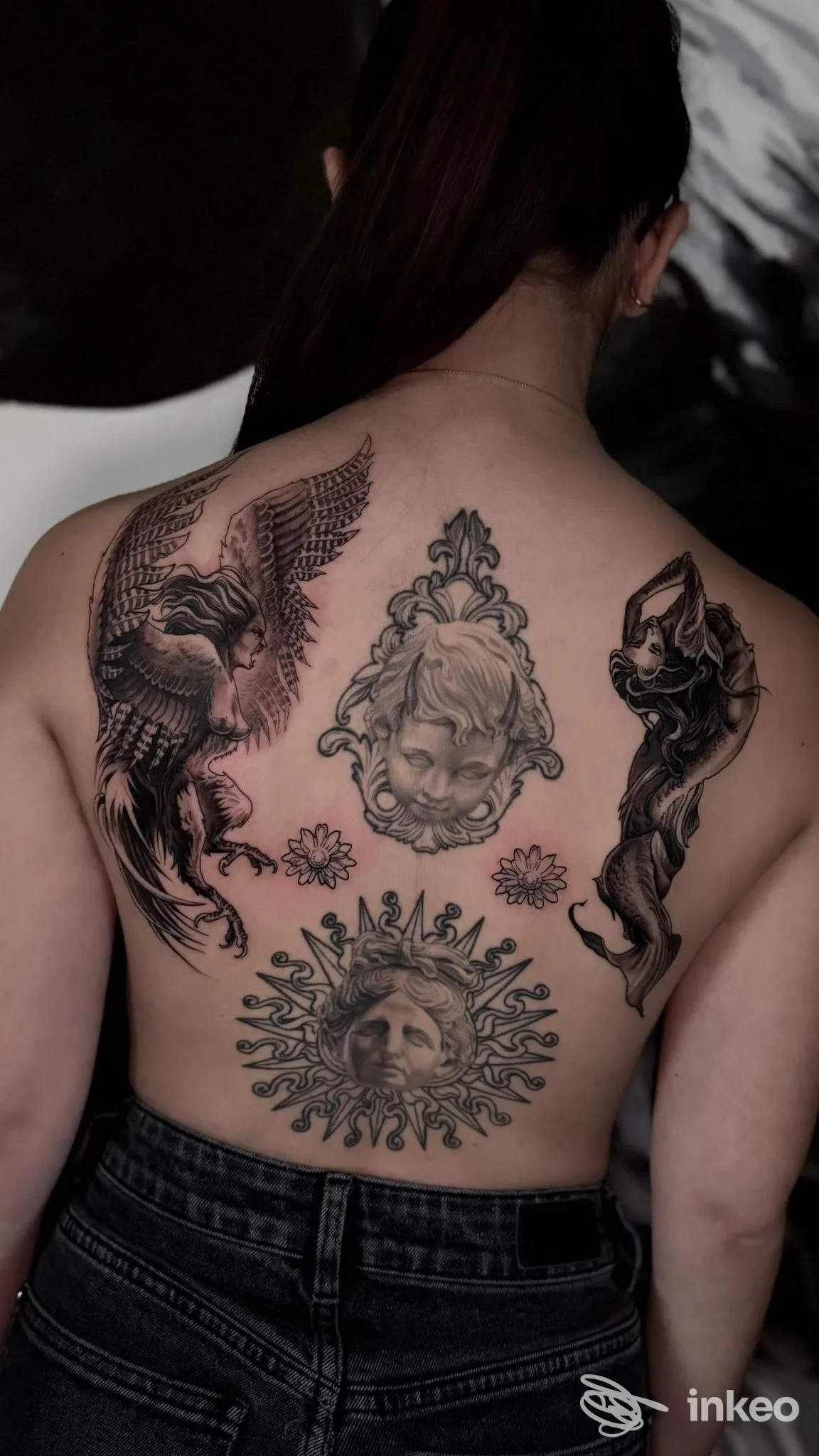 Dorso di una persona con tatto visibile: al centro una figura solare con volto, ai lati due animali stilizzati e una serie di elementi ornamental, tatuaggi chiari su pelle. Studio The Oven Tattoo Gallery, Taverna.