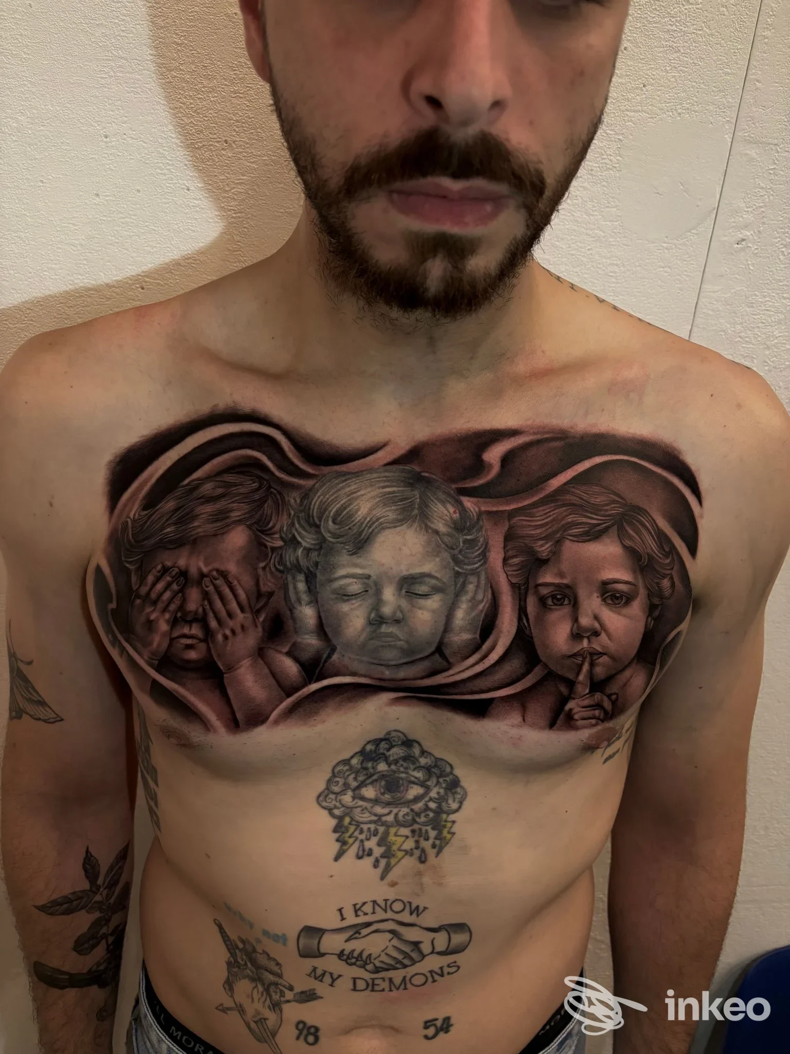 Tatuaggio sul torace raffigurante tre volti di bambini in tonalità scure, realizzato dallo studio Doca Tattoo a Gioia Tauro; si vede solo parte del viso dell’uomo, non l’intero volto, nessun overlay di social, nessuna immagine da schermo.