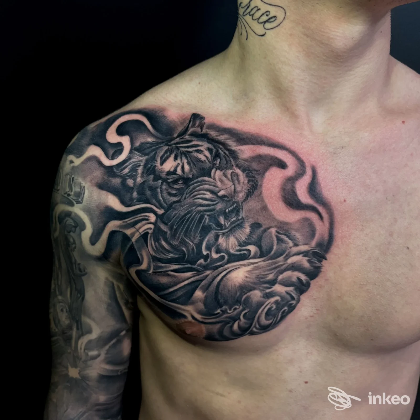 Tatuaggio nero e grigio su torace e spalla sinistra, realizzato sulla pelle; si distingue una figura di dragone con sfumature e onde.