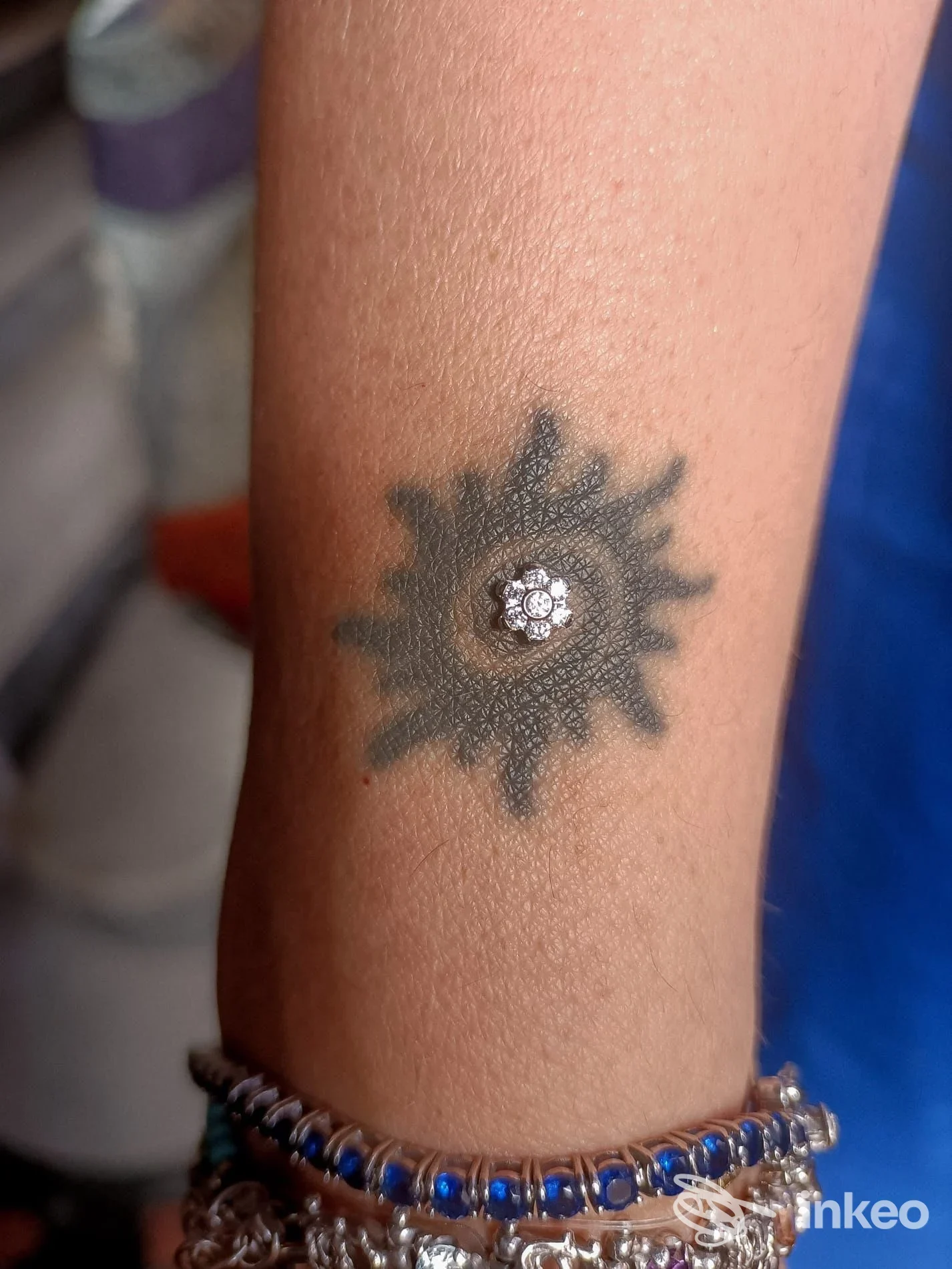 Tattoo sul braccio raffigurante un sole scuro con contorni sfumati e centro a forma di piccola decorazione floreale bianca.