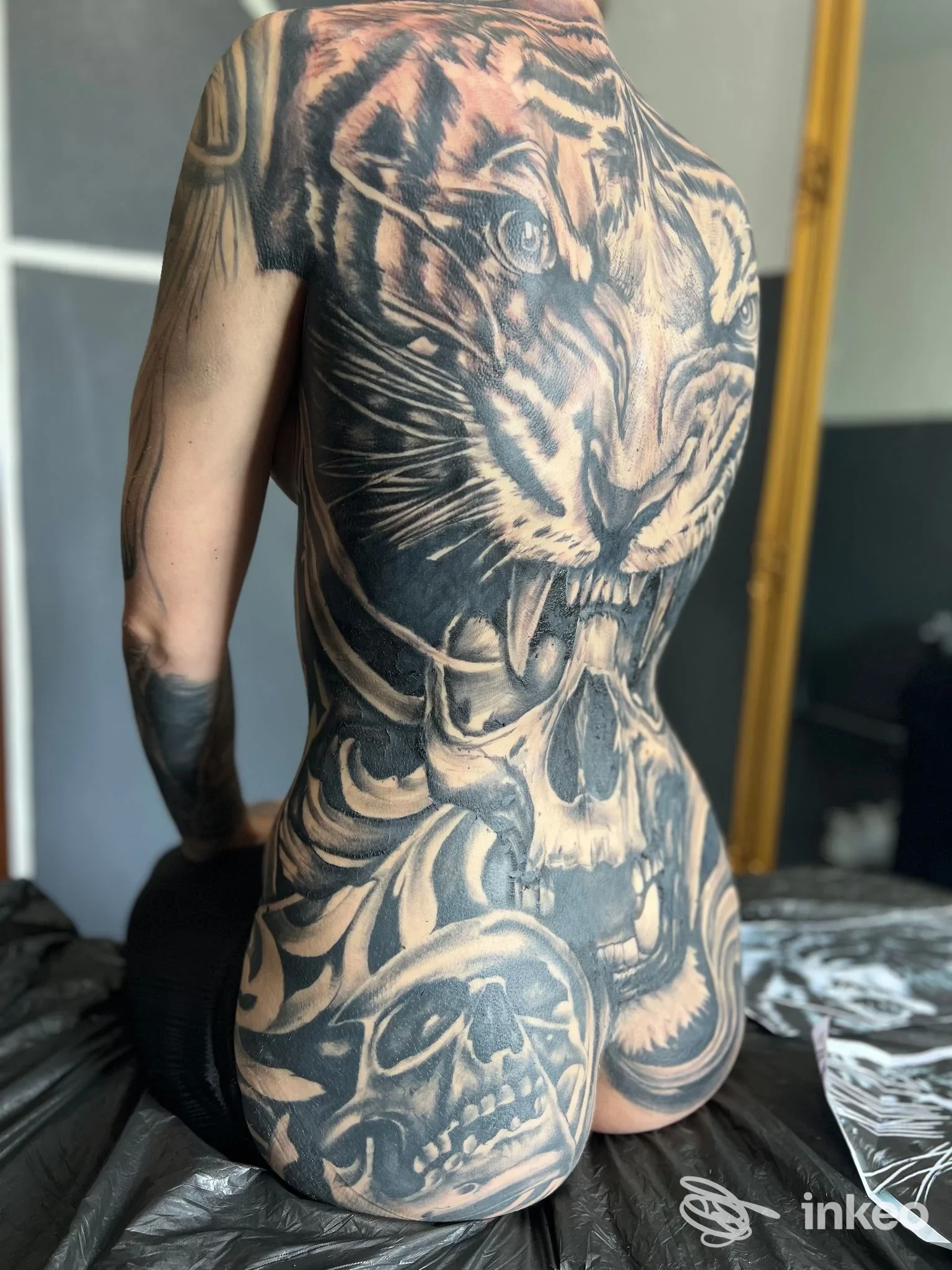 Tatuaggio realistico in bianco e nero su torace, schiena e glutei di una persona: tigre e teschi coprono ampie aree della pelle, stile realistico. Nessun overlay sociale o schermo visibile, volto non plenamente visibile.
