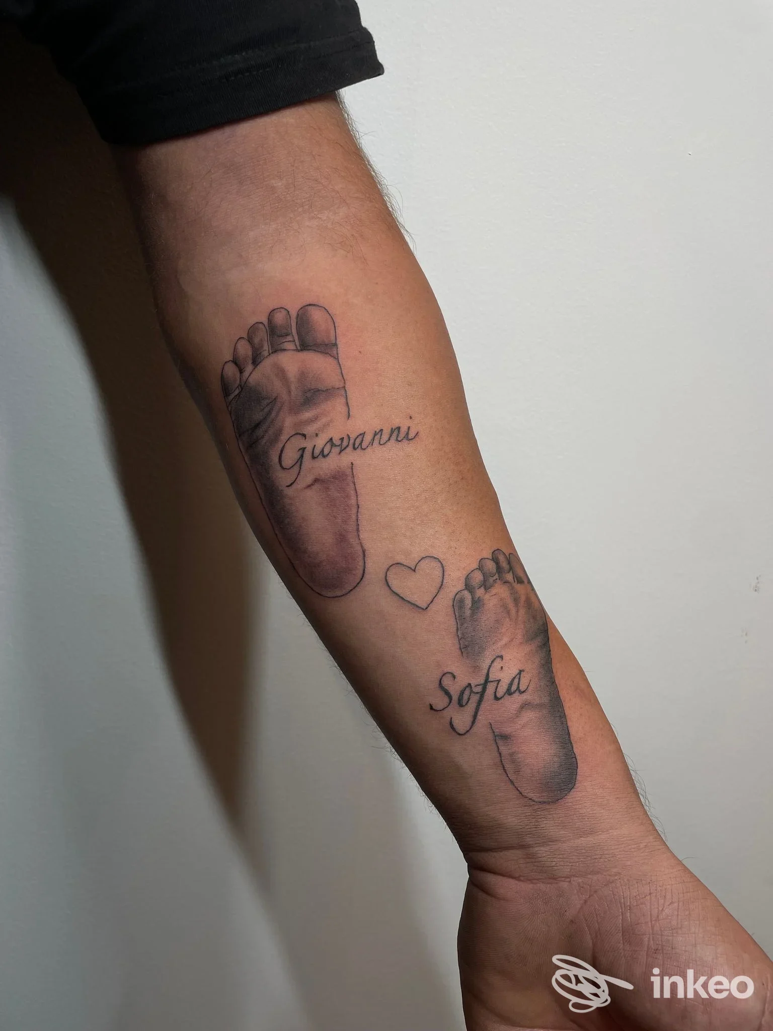 Avambraccio di una persona con due impronte di piede tatuate e due nomi Giovanni e Sofia, accanto a un piccolo cuore.