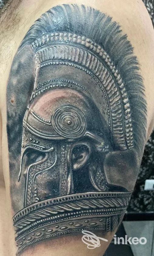 Tattoo realistico di elmo antico sul braccio, tonalità scure, dettagli scolpiti e sfumature realistiche. visibile pelle reale, senza volto.