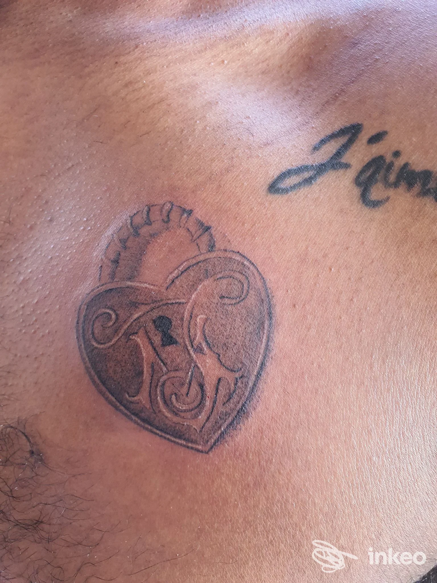 Tatuaggio sul torace raffigurante un cuore con lucchetto, linea scura e dettagli intricati, visibile sulla pelle, senza volto umano nelle vicinanze.