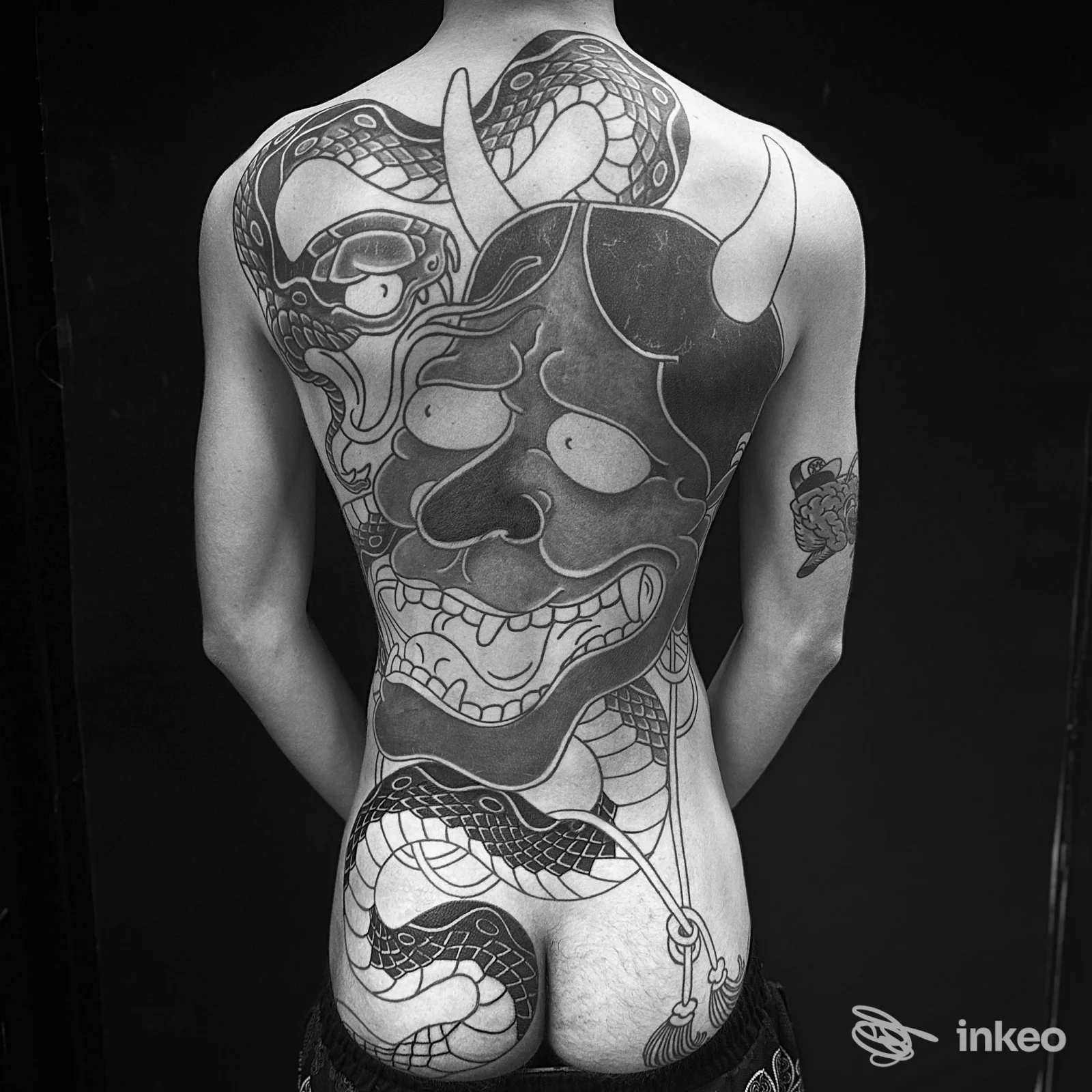 Tattoo esteso sulla schiena con dettagli intricati in toni nero/grigio, serpente e maschera, visibile senza volto. Studio Custom Tattoo BG.