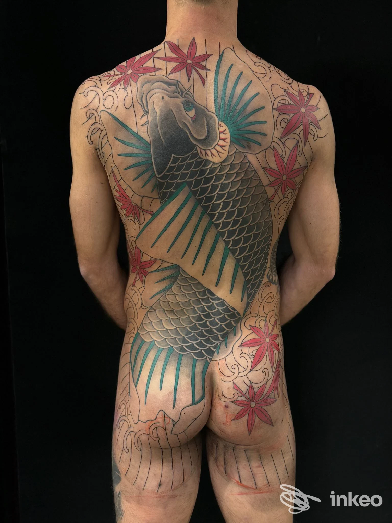 Schiena nuda con grande tatuaggio giapponese di pesce koi dalle pinne azzurre e fiori rossi, vista posteriore, senza volto.