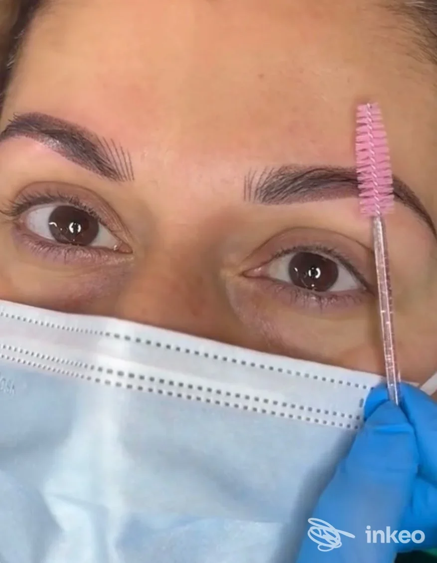 Primo piano di volto con mascherina chirurgica, sopracciglia tratte con trucco permanente in corso, spazzola rosa vicino all'arcata; eseguito da Francesca Ale Zappia a Gioia Tauro.