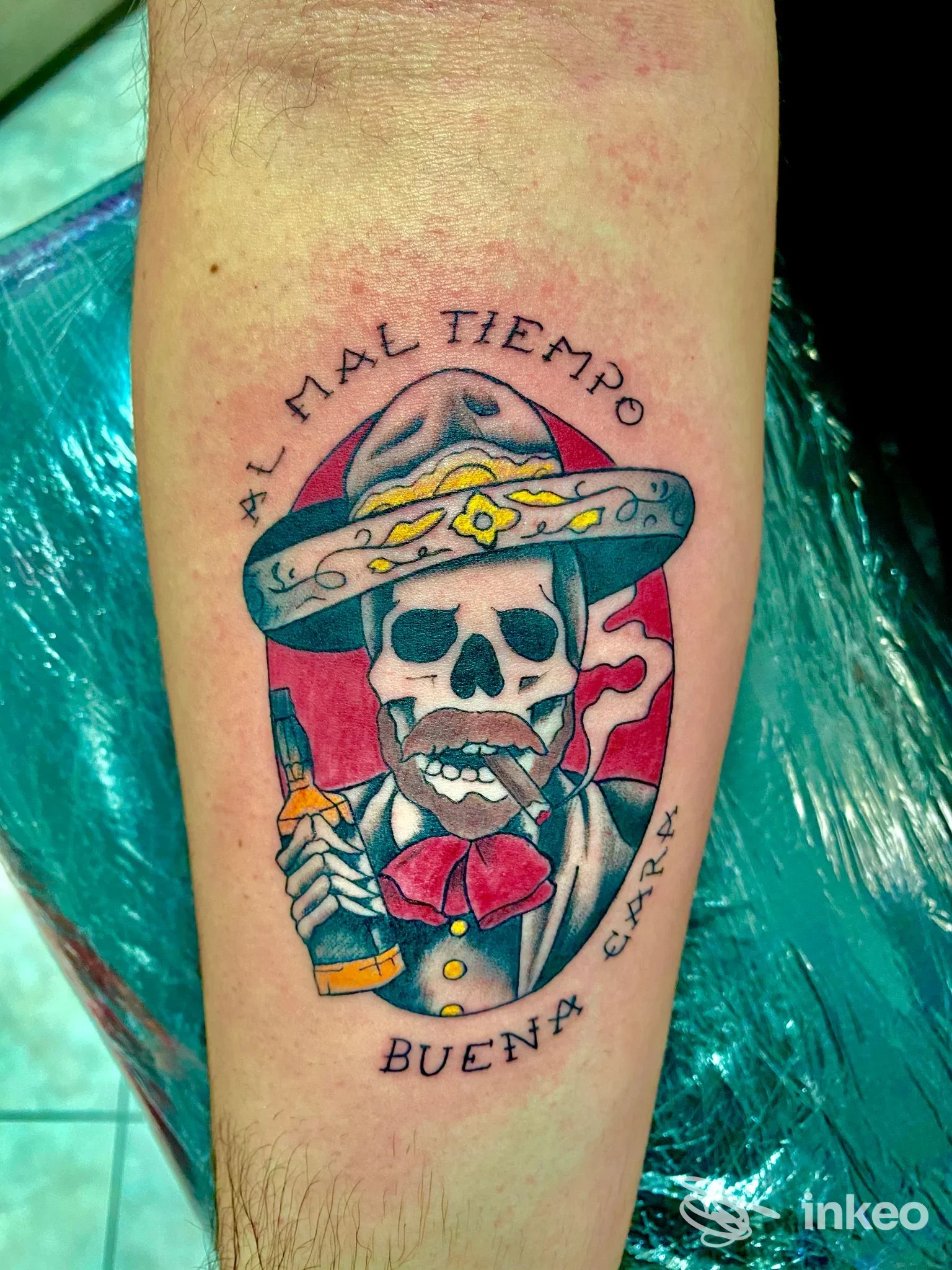 Tattoo su avambraccio raffigurante una testa di scheletro con sombrero e sigaretta, sfondo rosso, con scritte tonde attorno: Dreamink Tattoo Studio, Amantea, mostra colori vividi e linee nette.