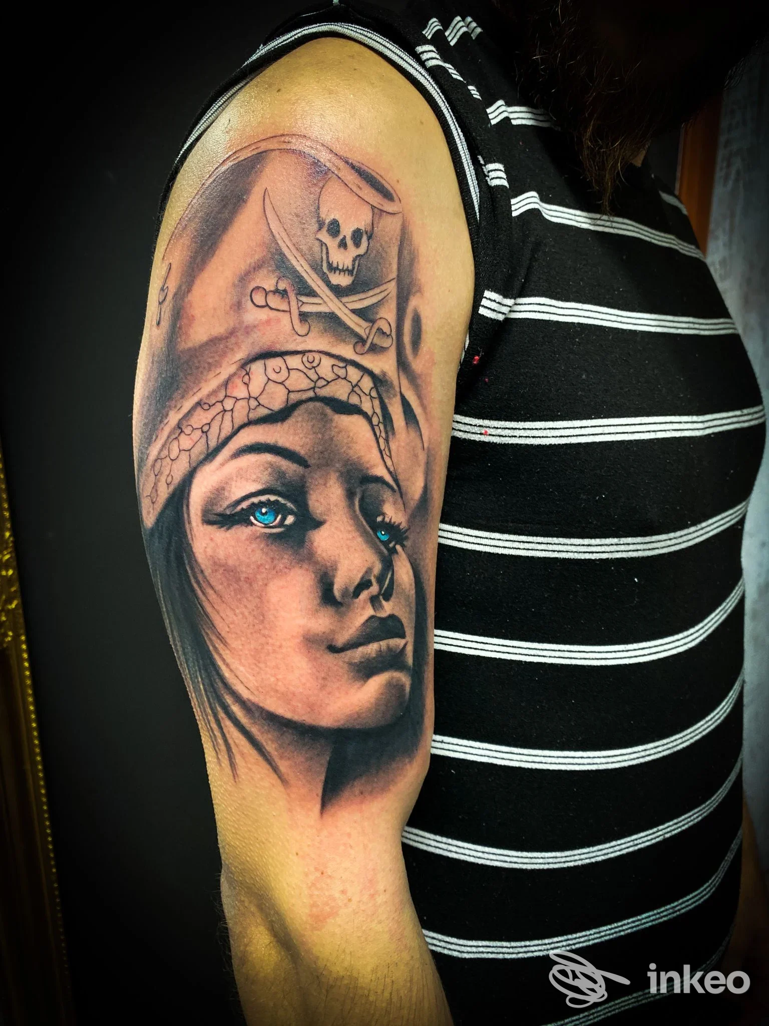 Tattoo realistico sul braccio raffigurante una donna con sfondo di teschio e croce, tinta in tonalità naturali e blu, area superiore del braccio, colori marcati e linee pulite.