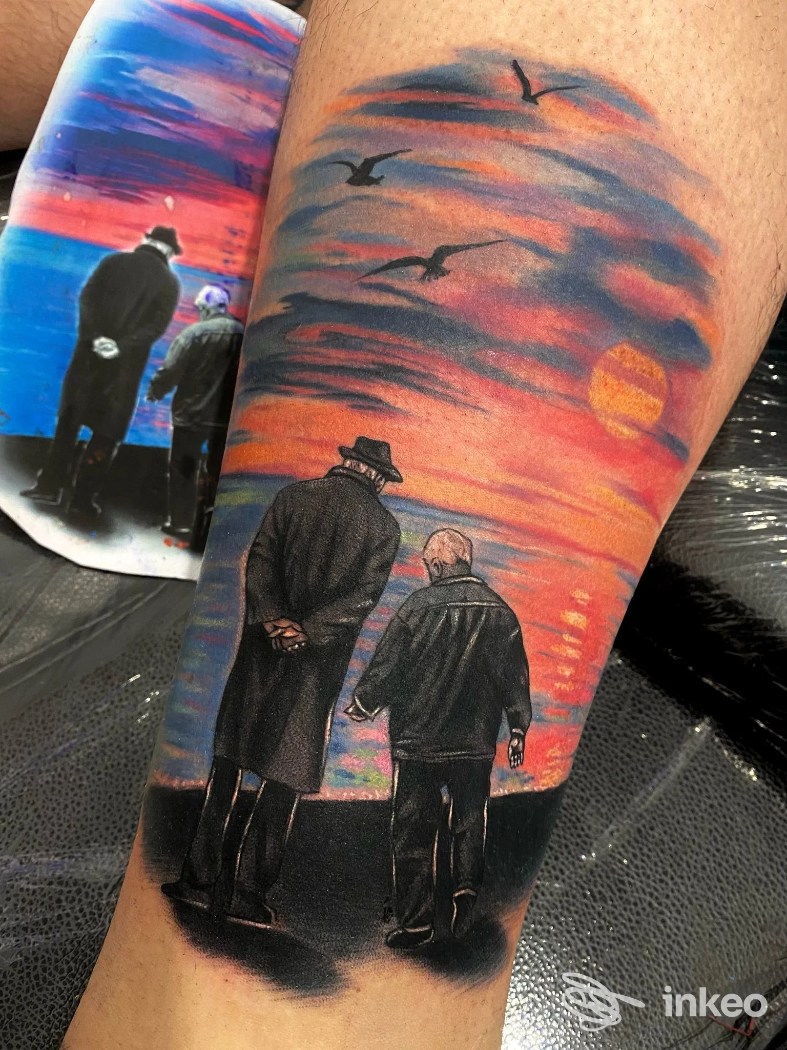 Tattoo sul braccio raffigurante due uomini visti di schiena davanti a un tramonto con gabbiani e sole arancione; realizzato da Dopamine Tattoo Studio a Diamante.