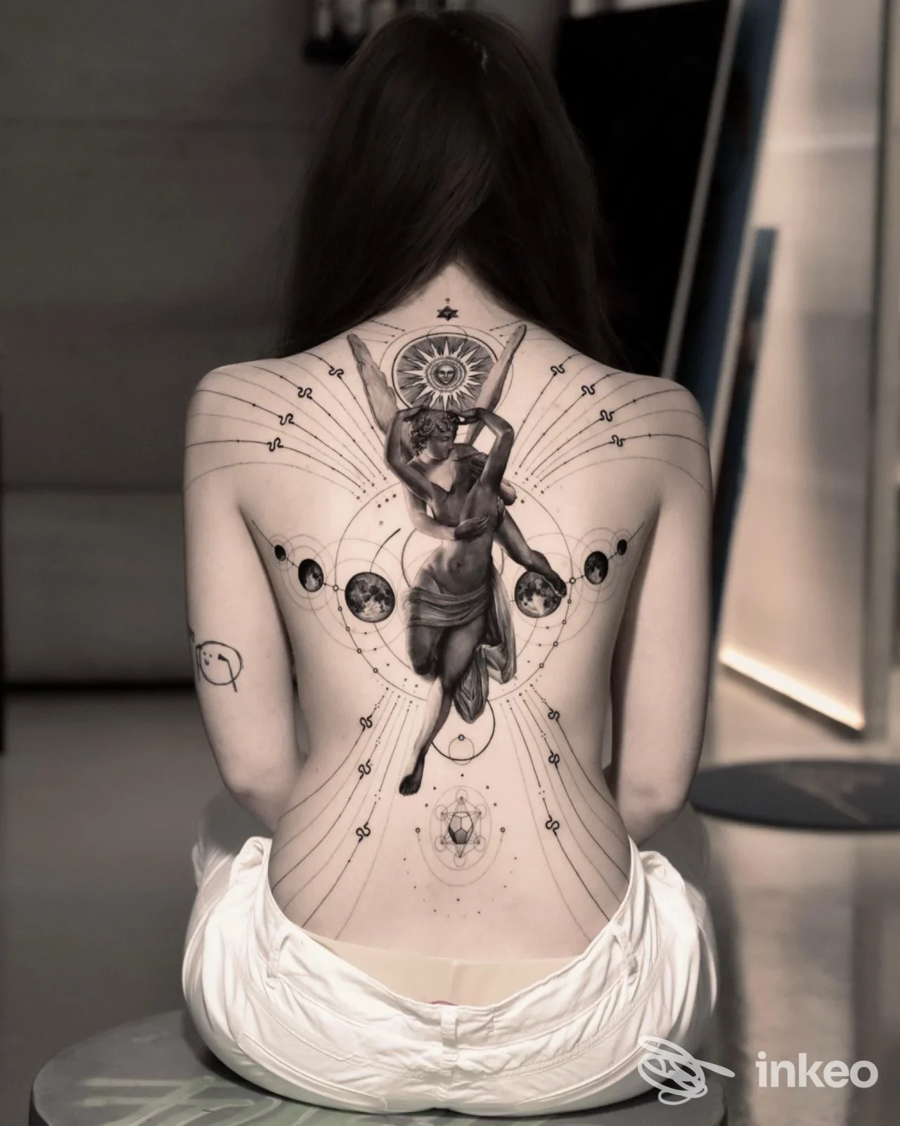 Schiena e spalle di una persona viste di schiena, con un grande tatuaggio realistico/ geometric. Dettagli: figura centrale e motivi astrali, senza testo o overlay social.