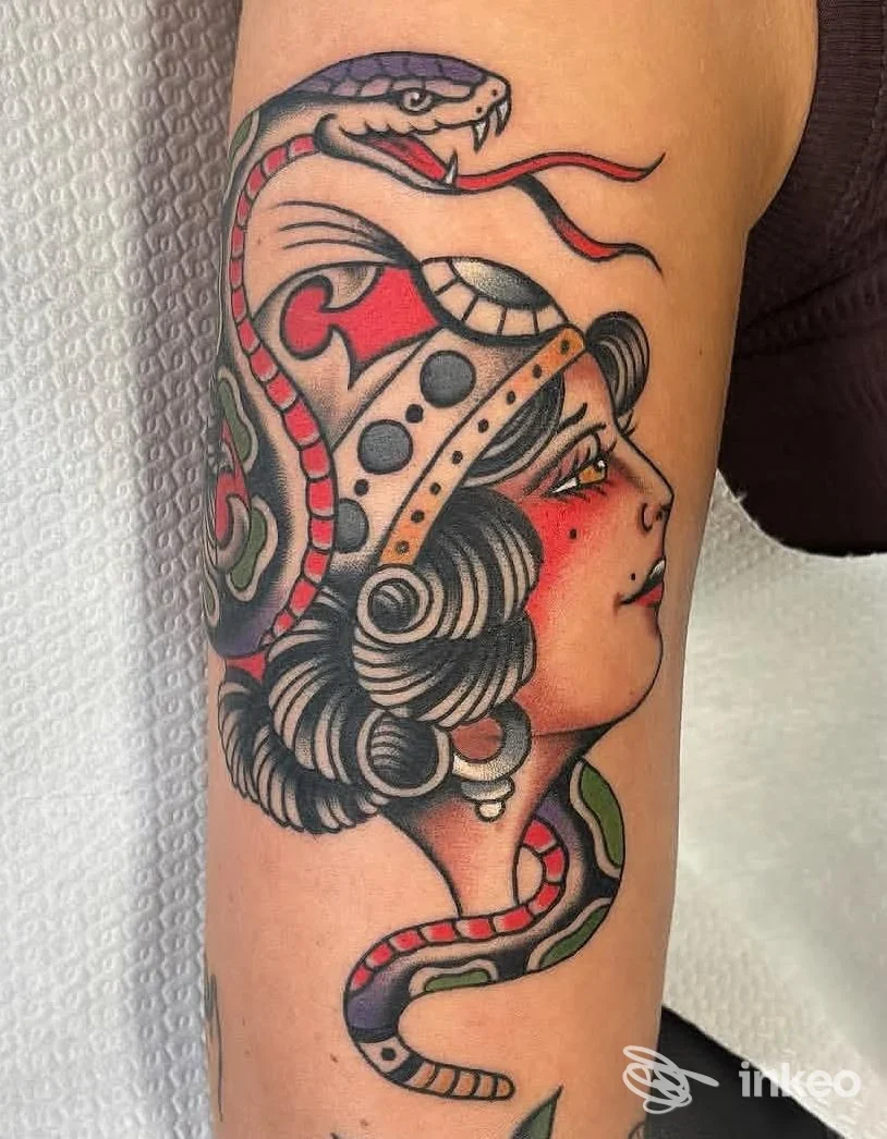 Tattoo visibile su avambraccio raffigurante profilo femminile con casco, serpente colorato avvolto intorno al braccio; stile tradizionale con contorni netti e colori vividi.