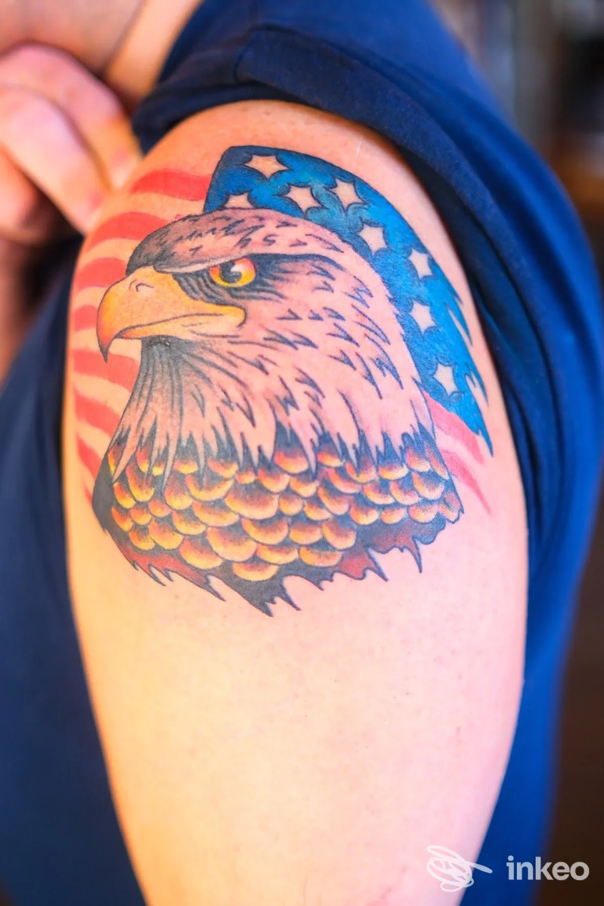 Tatuaggio sull'avambraccio raffigurante un'aquila colorata con sfondo a stelle e strisce, realizzazione corporea visibile.