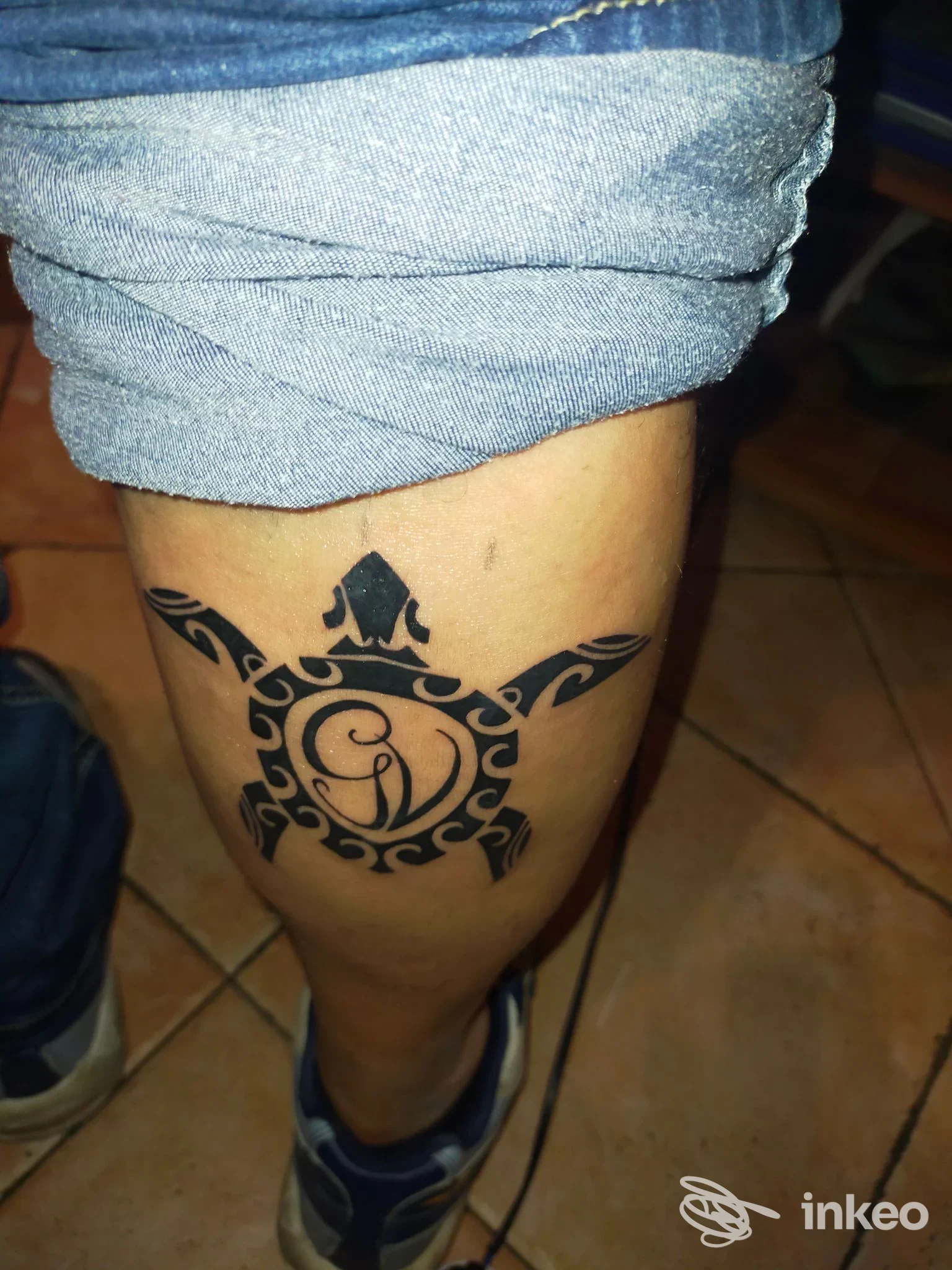 tattoo visibile sulla gamba, disegno in stile tribale con cerchio centrale; la pelle è in primo piano senza volto visibile, fascia scarpa e shorts lasciando visibile l'opera corporea.