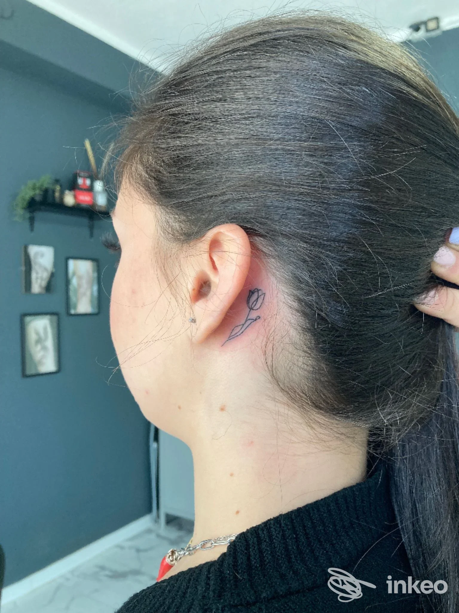 Piccola tatuatura a forma di rosa dietro l'orecchio sinistro di una persona, visibile su pelle reale, senza overlaid di social o immagine da schermo, in studio Blue Ink Studio, Praia a Mare.