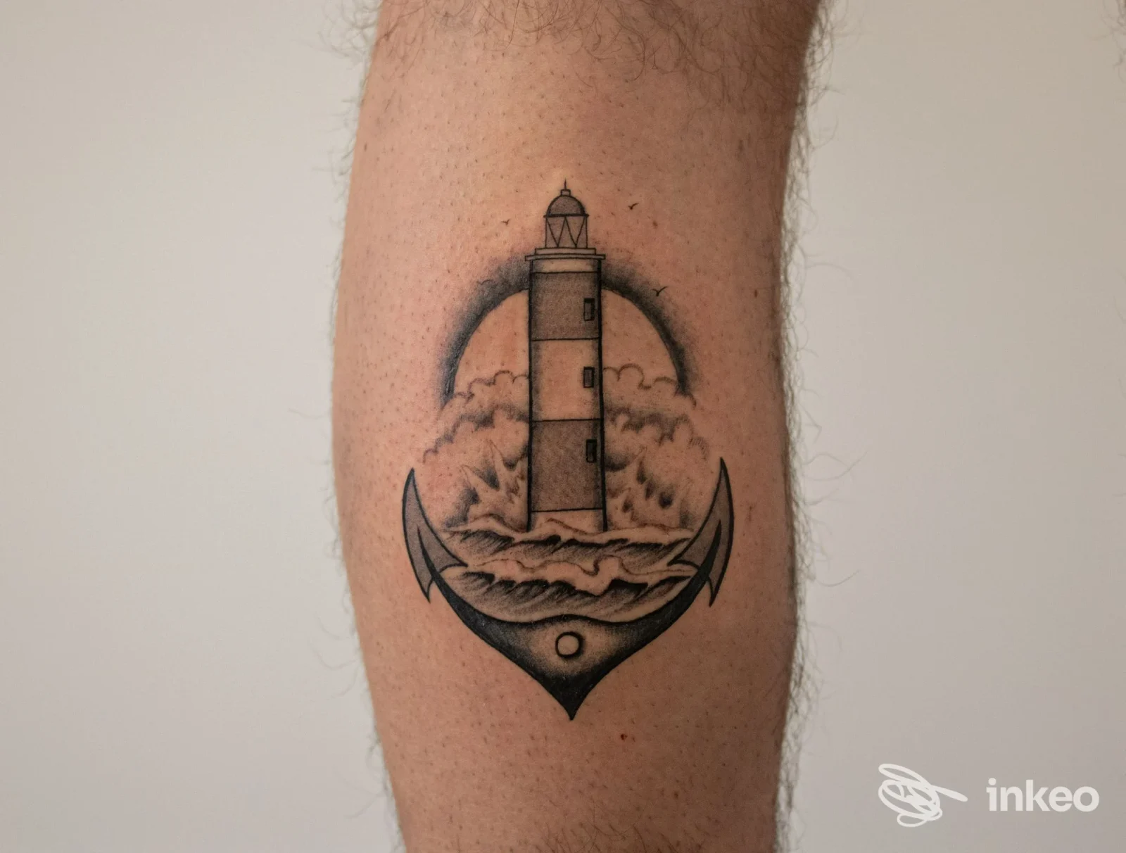 Tattoo sul braccio raffigurante un faro tra nuvole, con ancora stilizzata alla base; lavoro corporeo ben definito e in bianco e nero, di Daimon Tattoo, Villa San Giovanni.