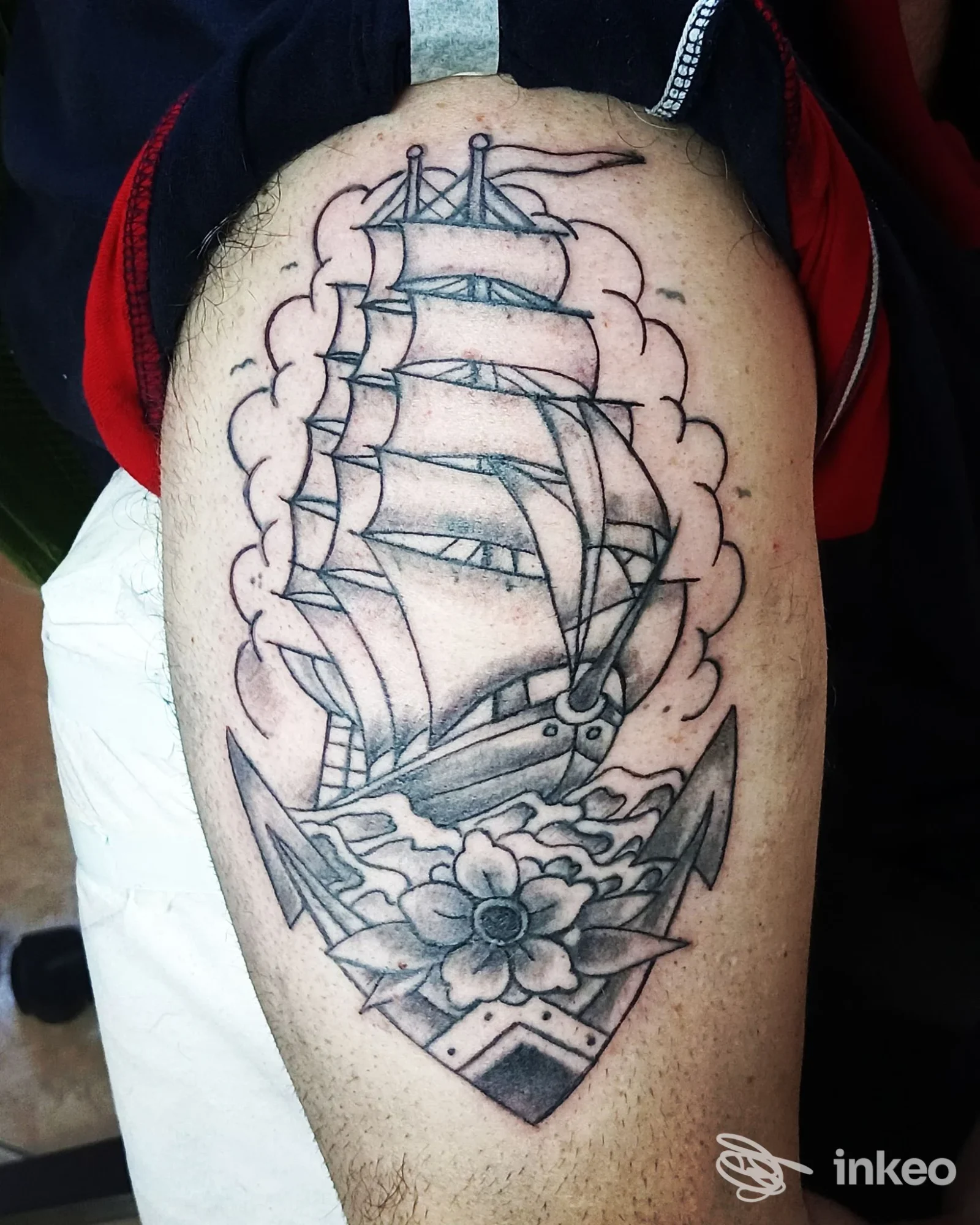 Tatuaggio realistico su pelle raffigurante una nave a vela con anfore e margherita, su gamba, in-line con linee di contorno e sfumature grigie-nerie.