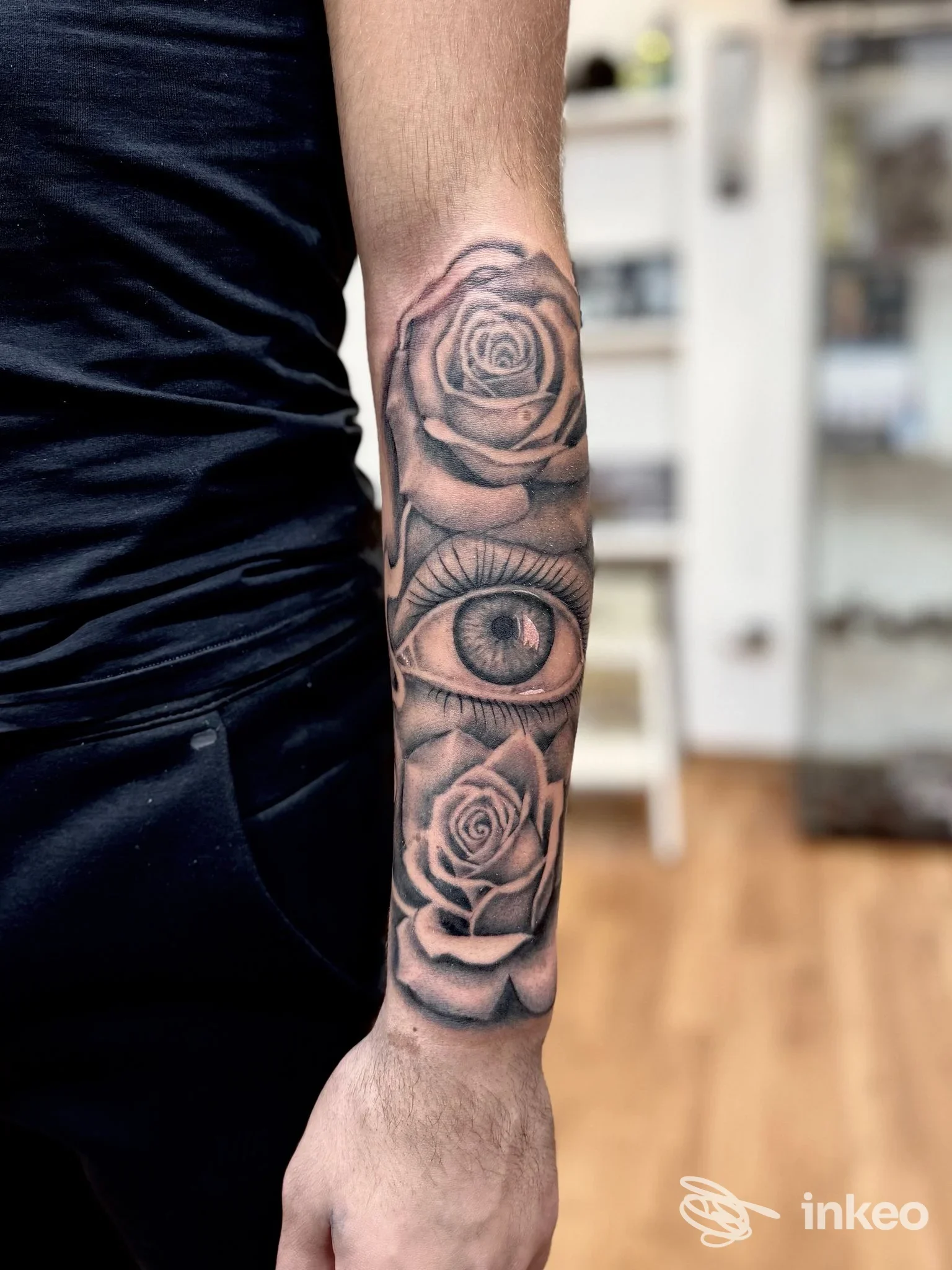 Braccio visibile con tatuaggio realistico in bianco e nero: rilievi di rose e un occhio lungo l’avambraccio, sfondo sfocato in studio South Blood Tattoo a Soverato.