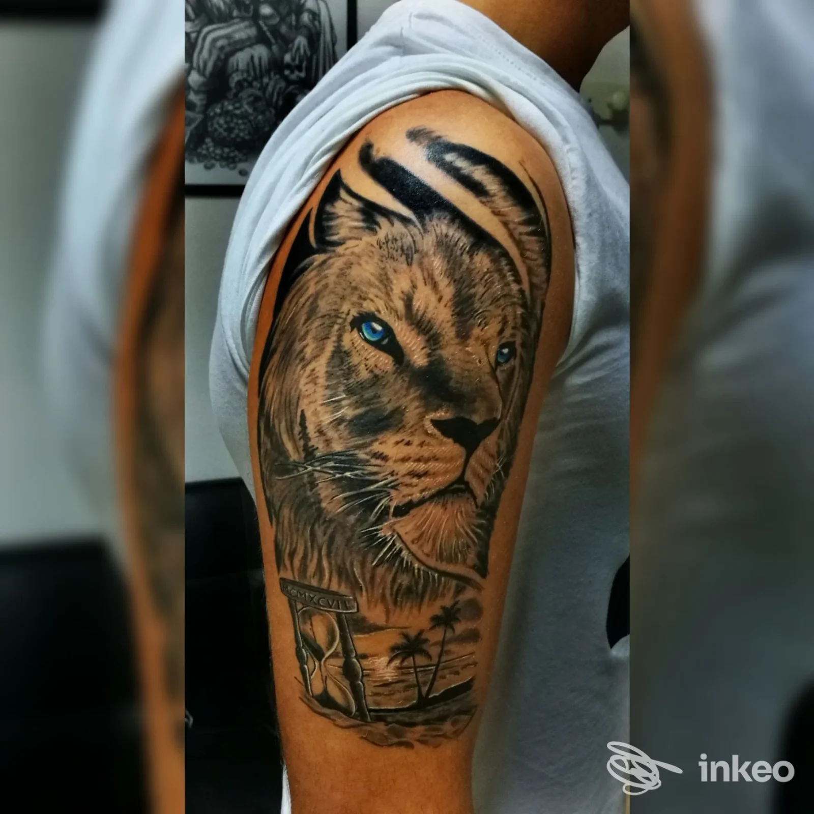 Tattoo sul braccio raffigurante un leone realistico con piercing olandato: colori terrosi, dettaglio del manto, occhio azzurro, con sfondo paesaggistico in bianco e nero; stile realistico, eseguito da La Perla Nera Tattoo a Botricello.