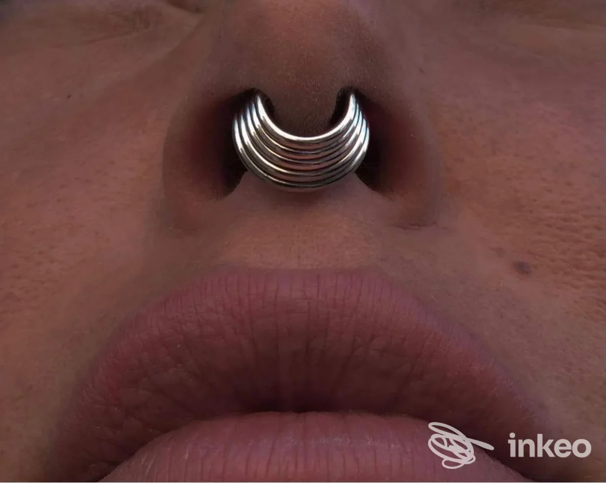 Inserimento di un piercing al naso a forma semicircolare in metallo, visibile sul volto di una persona; focus su narice e labbra senza mostrare l’intero viso.