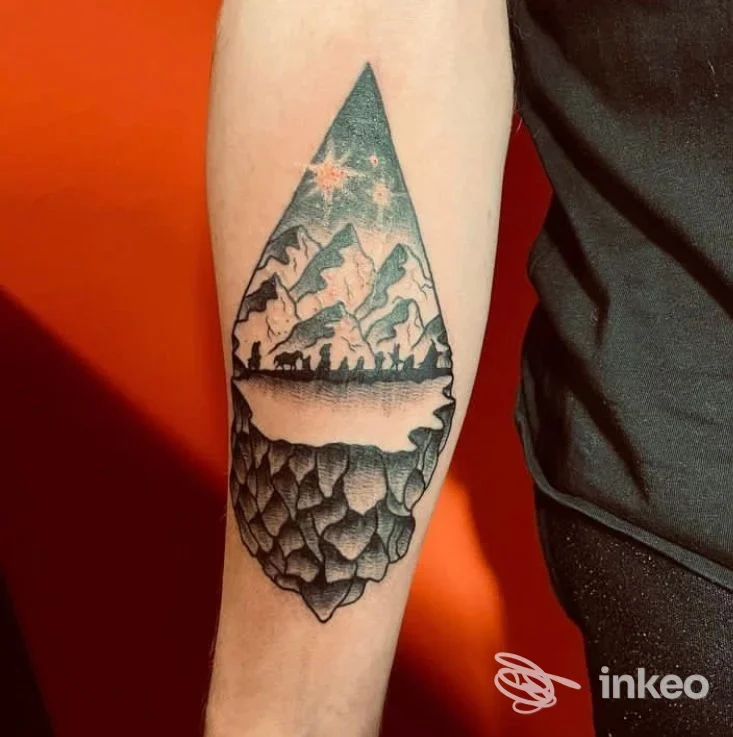 Tatuaggio geometrico a forma di triangolo sul braccio, con paesaggio montuoso e lago in tonalità nere su pelle chiara.