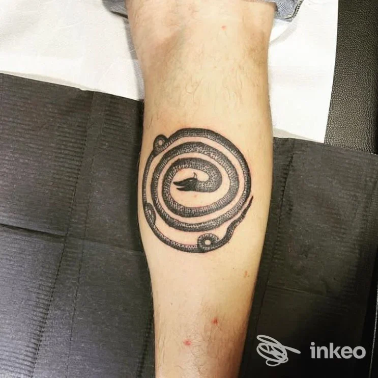 Tatuaggio nero a spirale circolare sulla pelle dell’avambraccio, realizzato con linee spesse e contorni netti.
