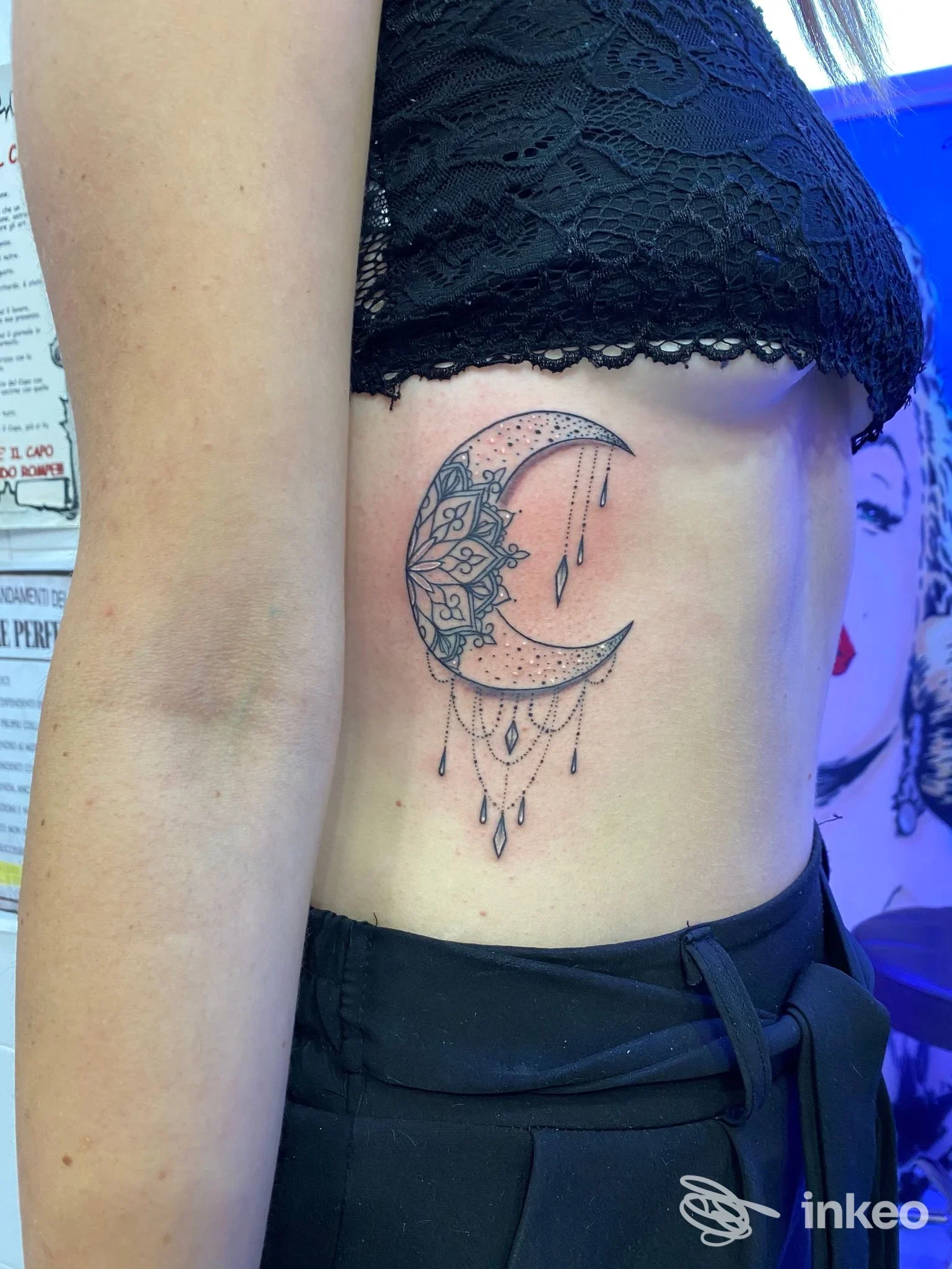 Tattoo sul fianco sinistro: luna crescente con motivo mandala e pendenti a goccia, eseguito in inchiostro nero.
