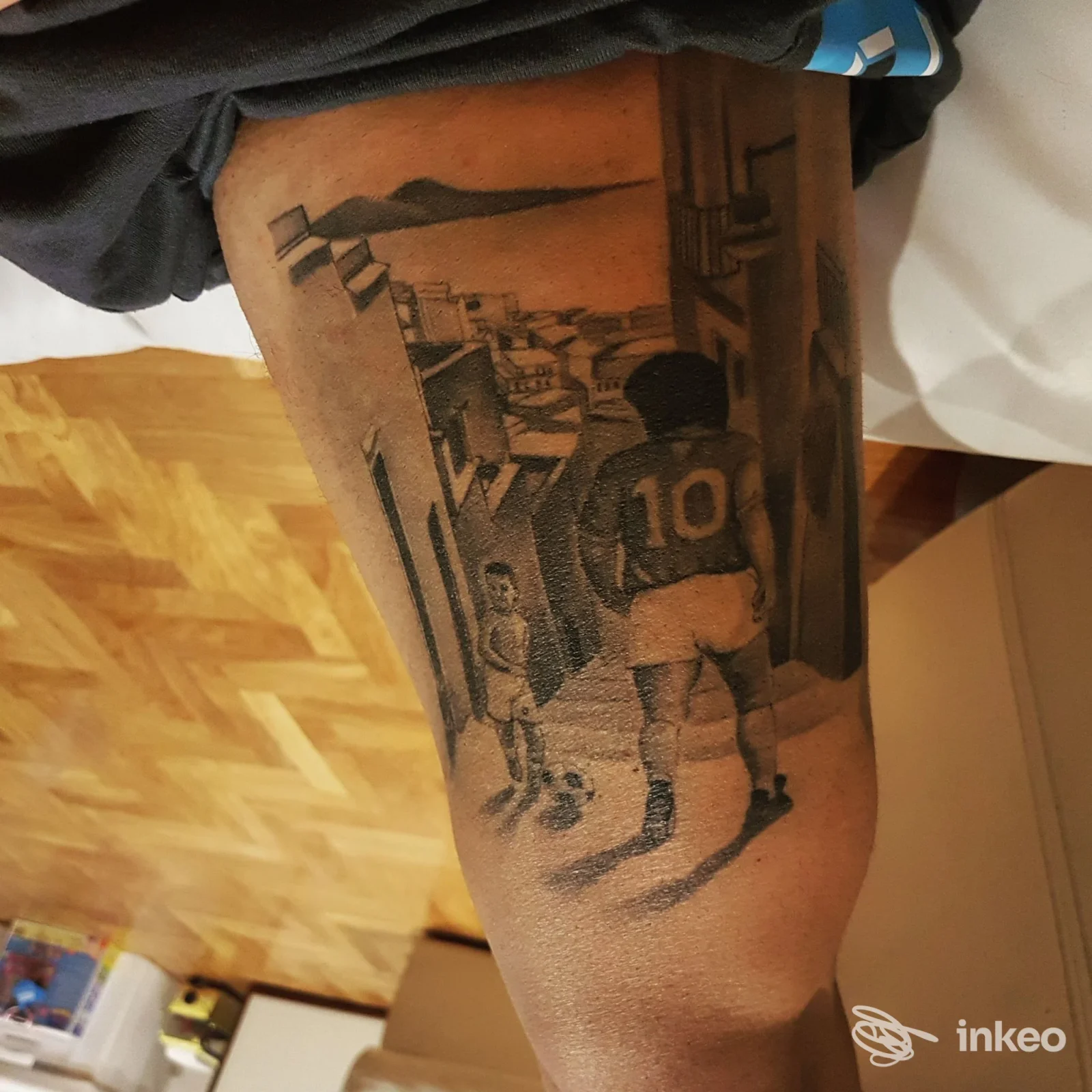 Tattoo realistico monocromo su gamba, figura di bambino con maglia numero 10, sfondo urbano, visibile solo la parte inferiore del corpo senza volto