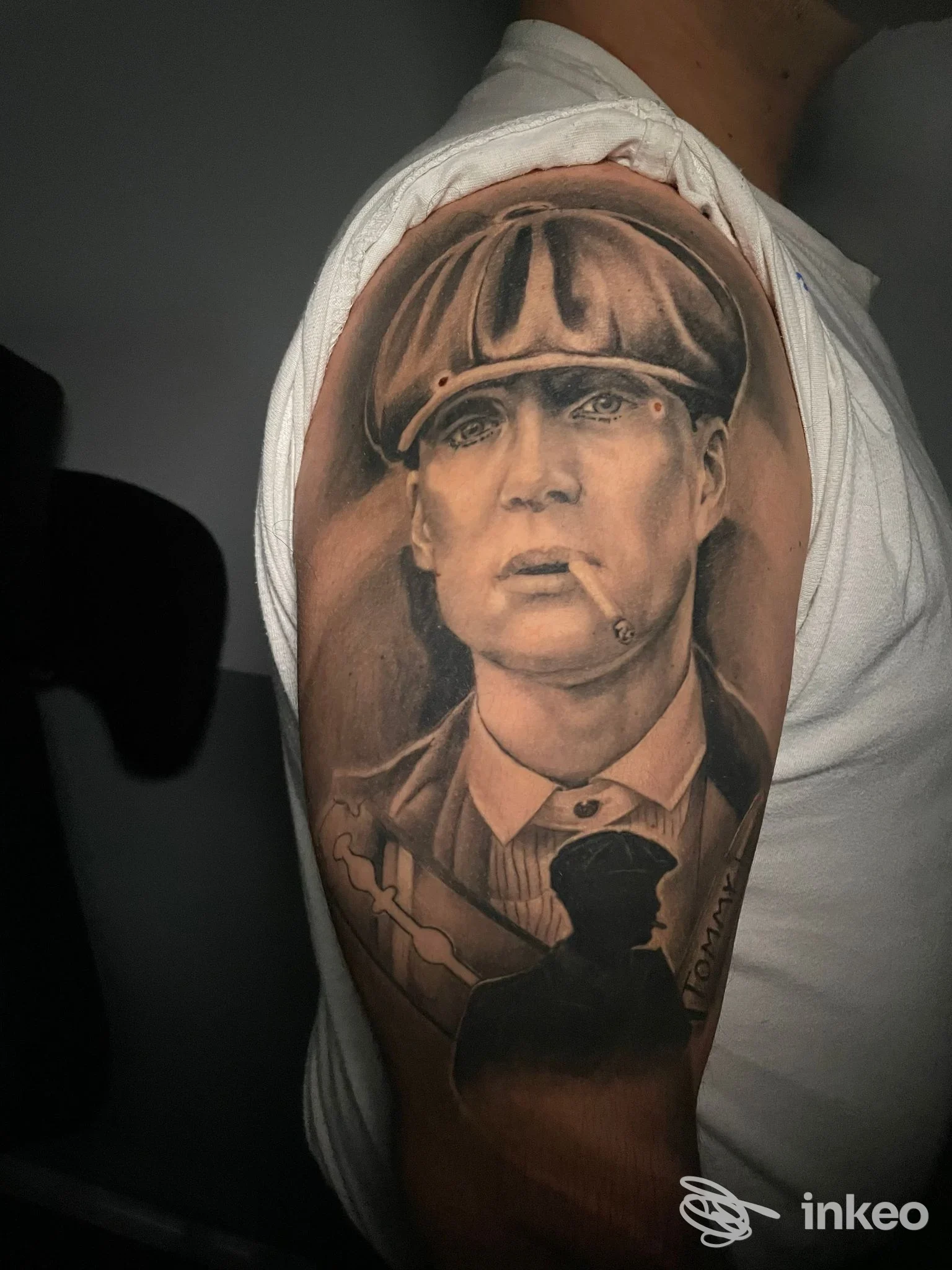 Tattoo realistico sull'avambraccio raffigurante un uomo con berretto, realizzato in tonalità sombre su pelle chiara, con dettagli di luci e ombre.