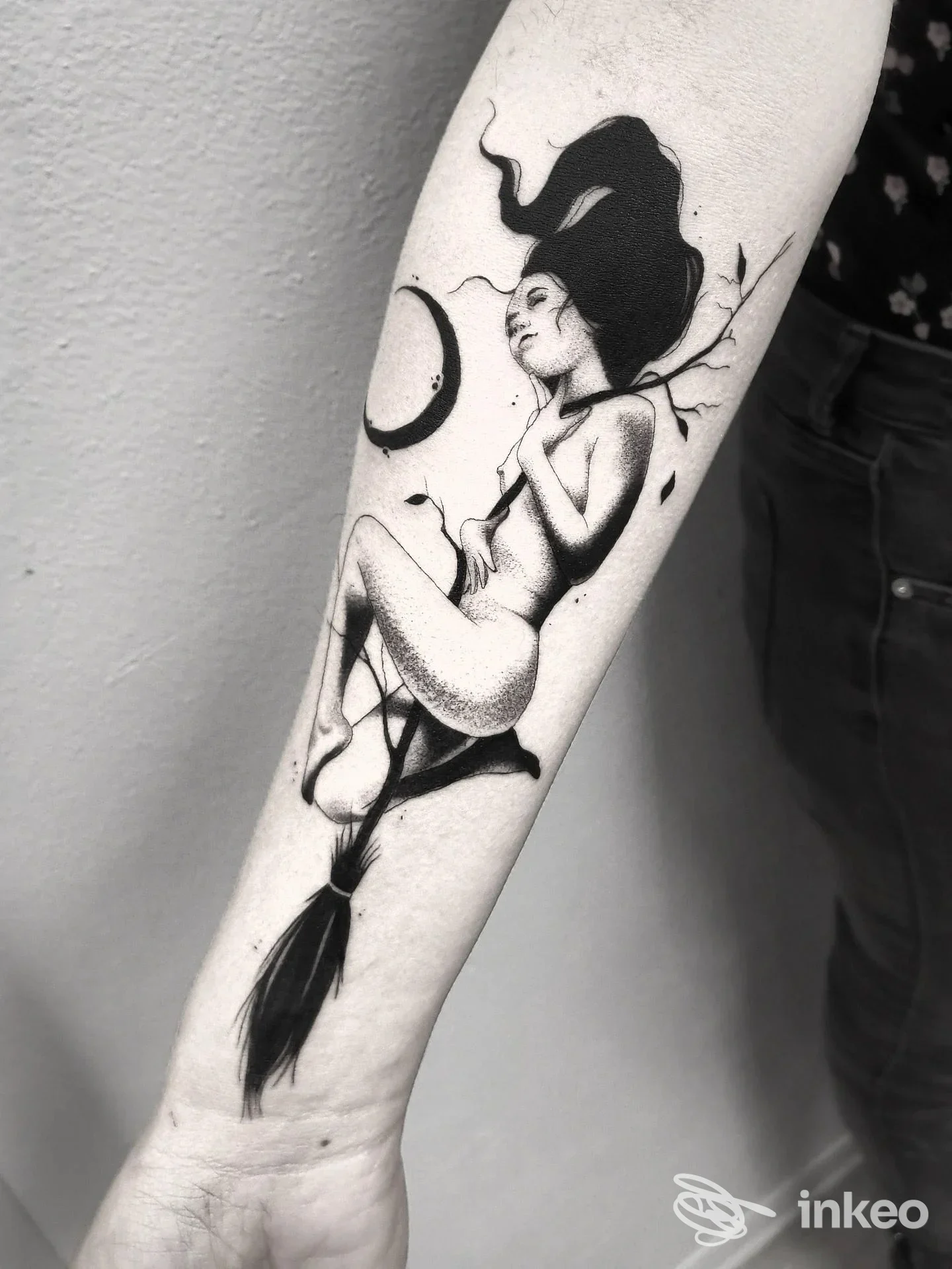 Avambraccio di una persona con tatuaggio in bianco e nero raffigurante una figura femminile stilizzata, con capelli fluenti e luna crescente sullo sfondo.