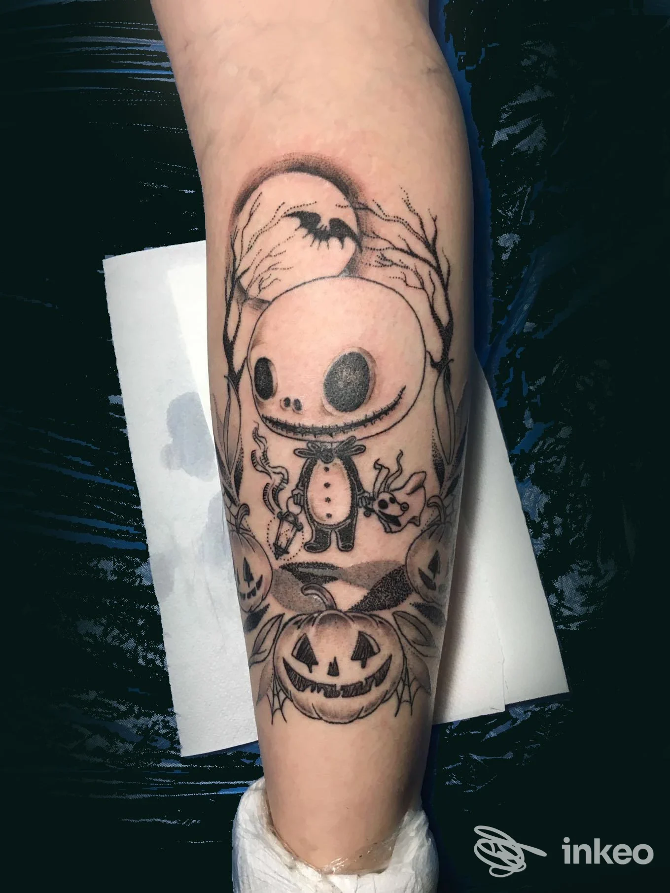 Tattoo sul braccio raffigurante un personaggio in stile macabro-astratto con luna e zucche, linee nere su pelle chiara, con dettaglio di ombre e cornici. Napoli, studio Solve et Coagula Tattoo.