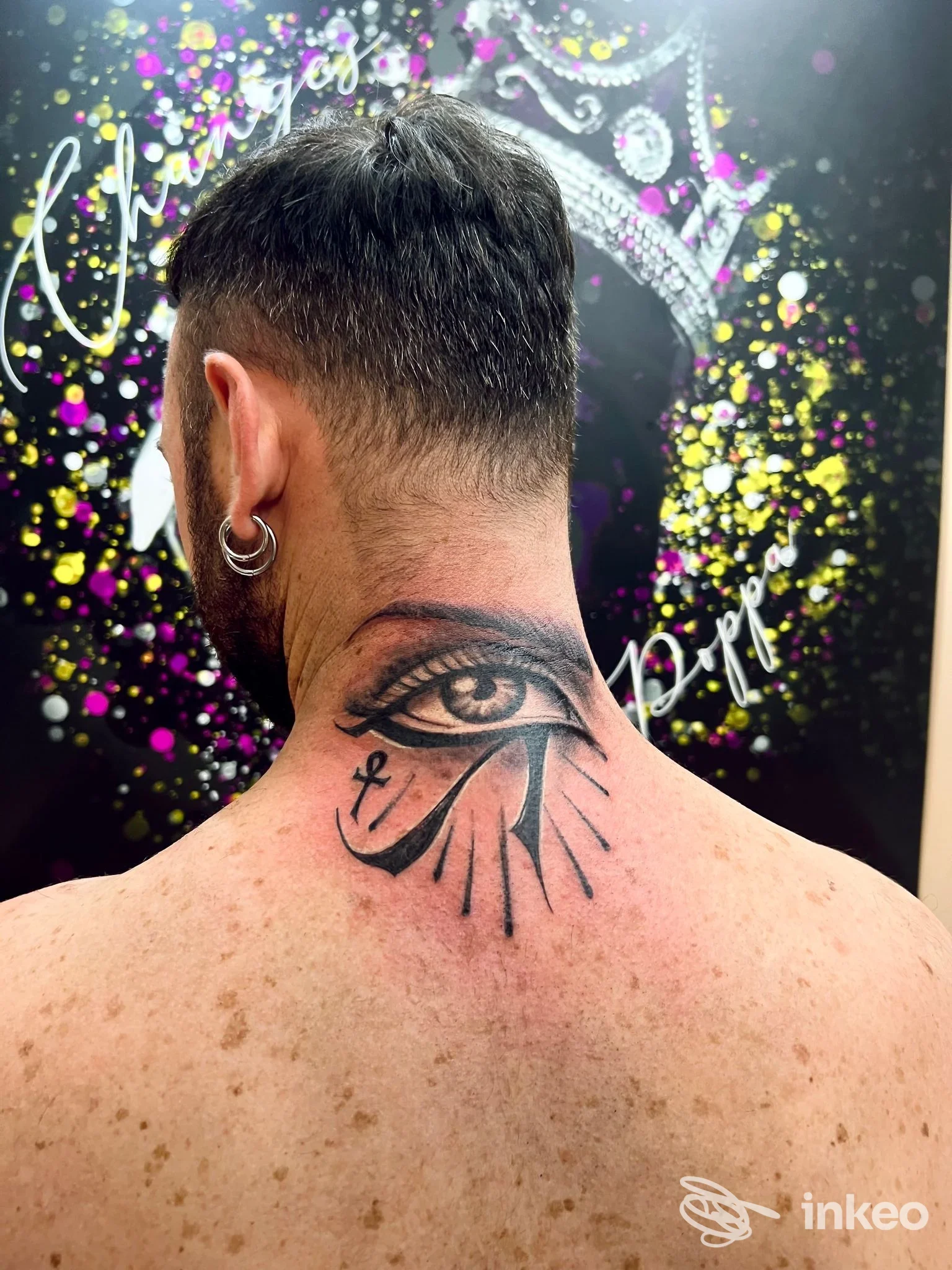 Tattoo sul retro del collo: un occhio stilizzato con raggi, eseguito sulla nuca/parte alta della schiena. sfondo di studio colorato.