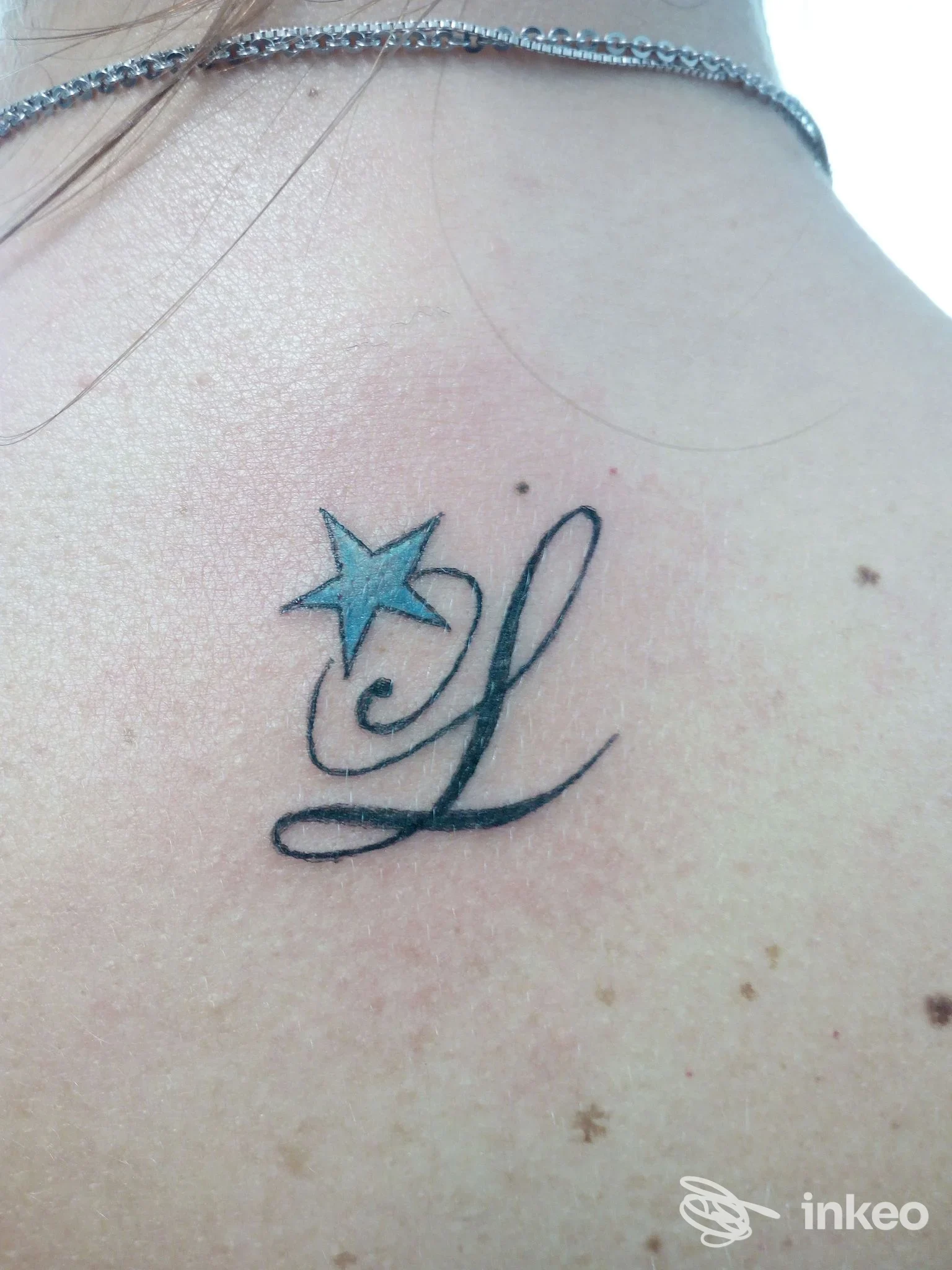 Tatuaggio sulla spalla visibile: una stella azzurra accanto a una lettera stilizzata L in nero, con pelle leggermente arrossata attorno al tatuaggio.