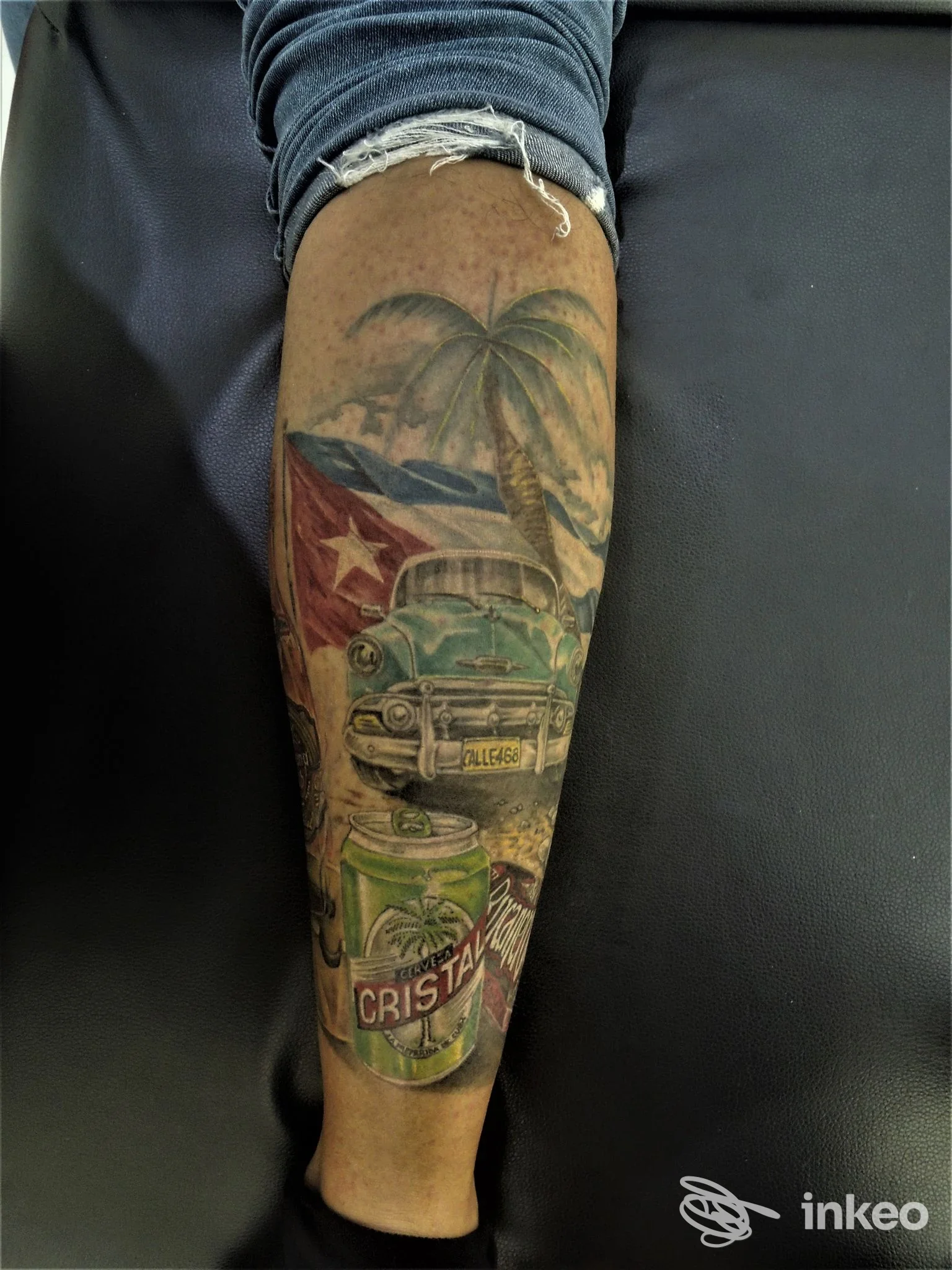 Tatuaggio realistico sul braccio raffigurante una palma, una vettura d’epoca e una lattina, con uno sfondo tropicale; realizzato presso TatuArti Studio InkMaster a Caivano, Italia.