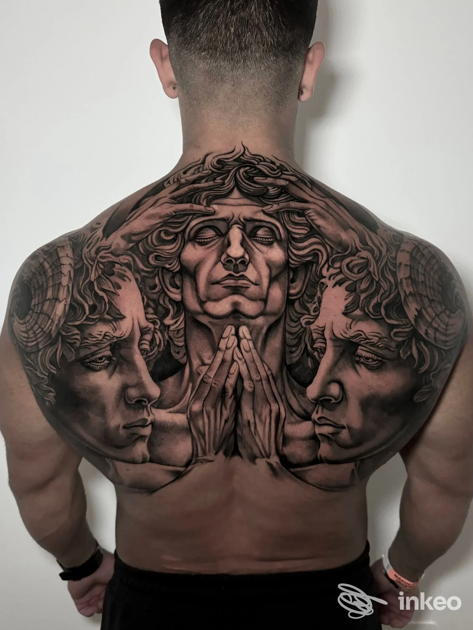 Grande tatuaggio sulla schiena e sulle spalle di un uomo: figure stilizzate di volti e mani unite, in stile realistico bianco e nero, riempie la schiena.