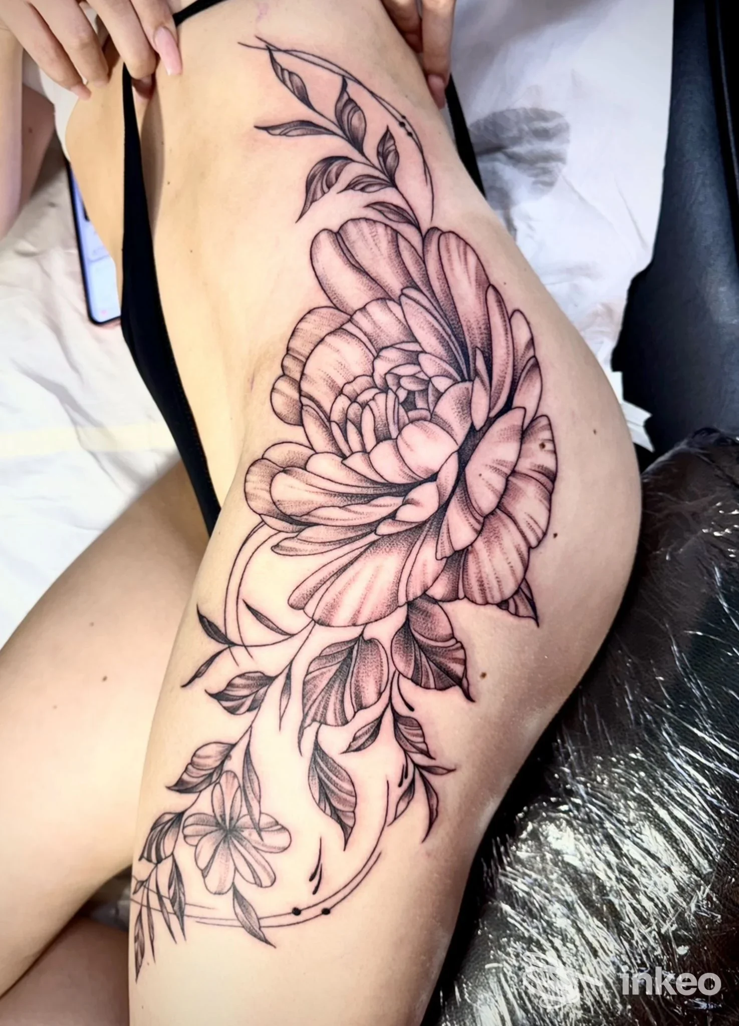 Tattoo floreale su coscia, disegno in bianco e nero con linee fini e sfumature, visibile sulla gamba.