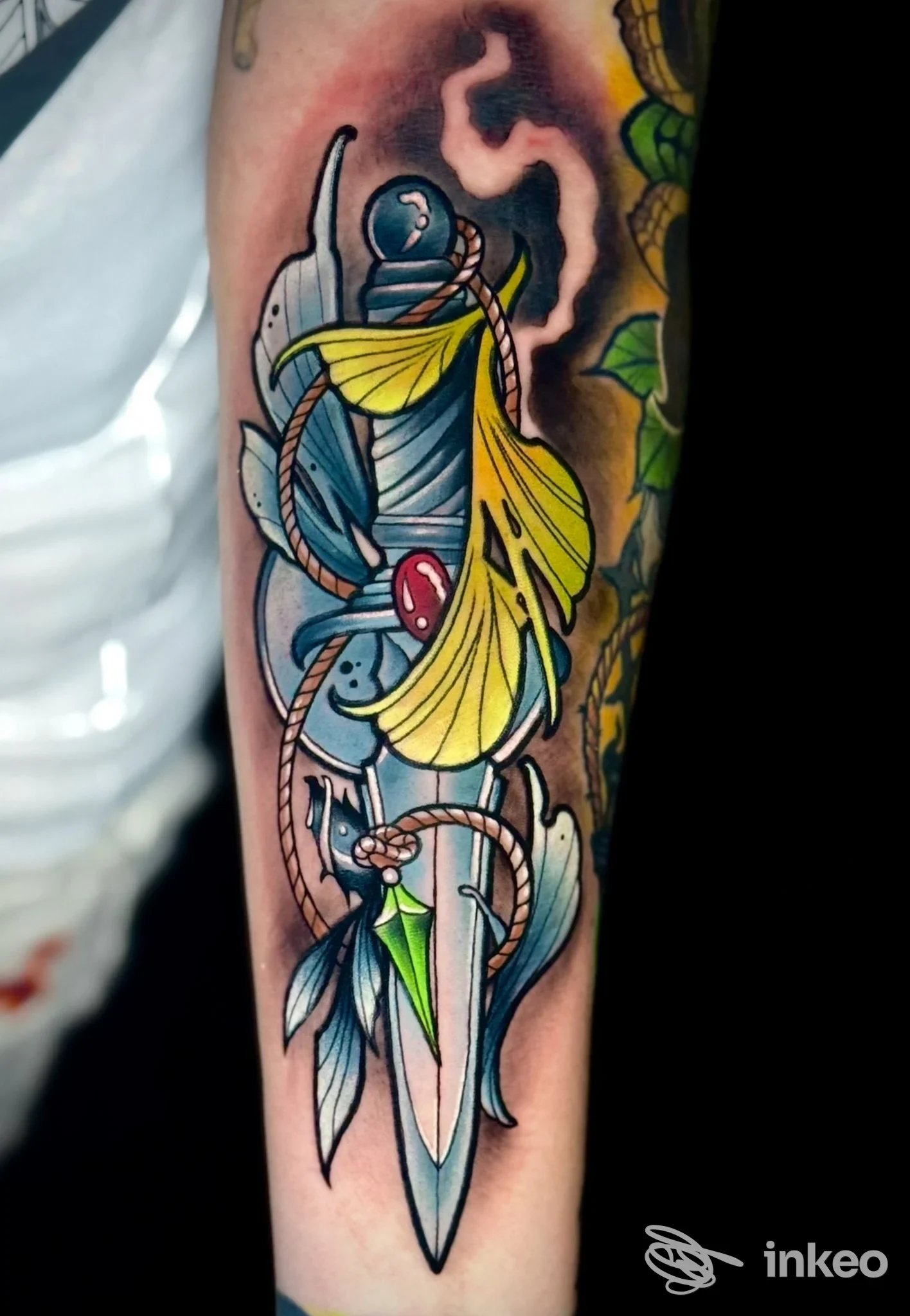 Tattoo colorato su avambraccio: lama, nastri gialli e dettagli azzurri in stile tradizionale; immagine singola senza testi o watermark.