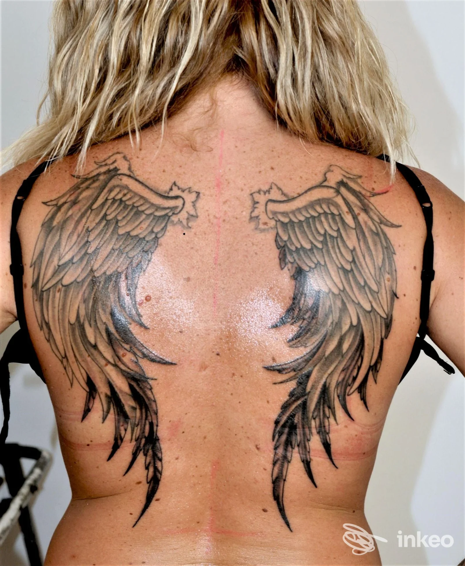 Tattoo reale di due ali stilizzate sulle scapole, visibile sulla schiena di una persona, con colori neri e grigi e linee nette.