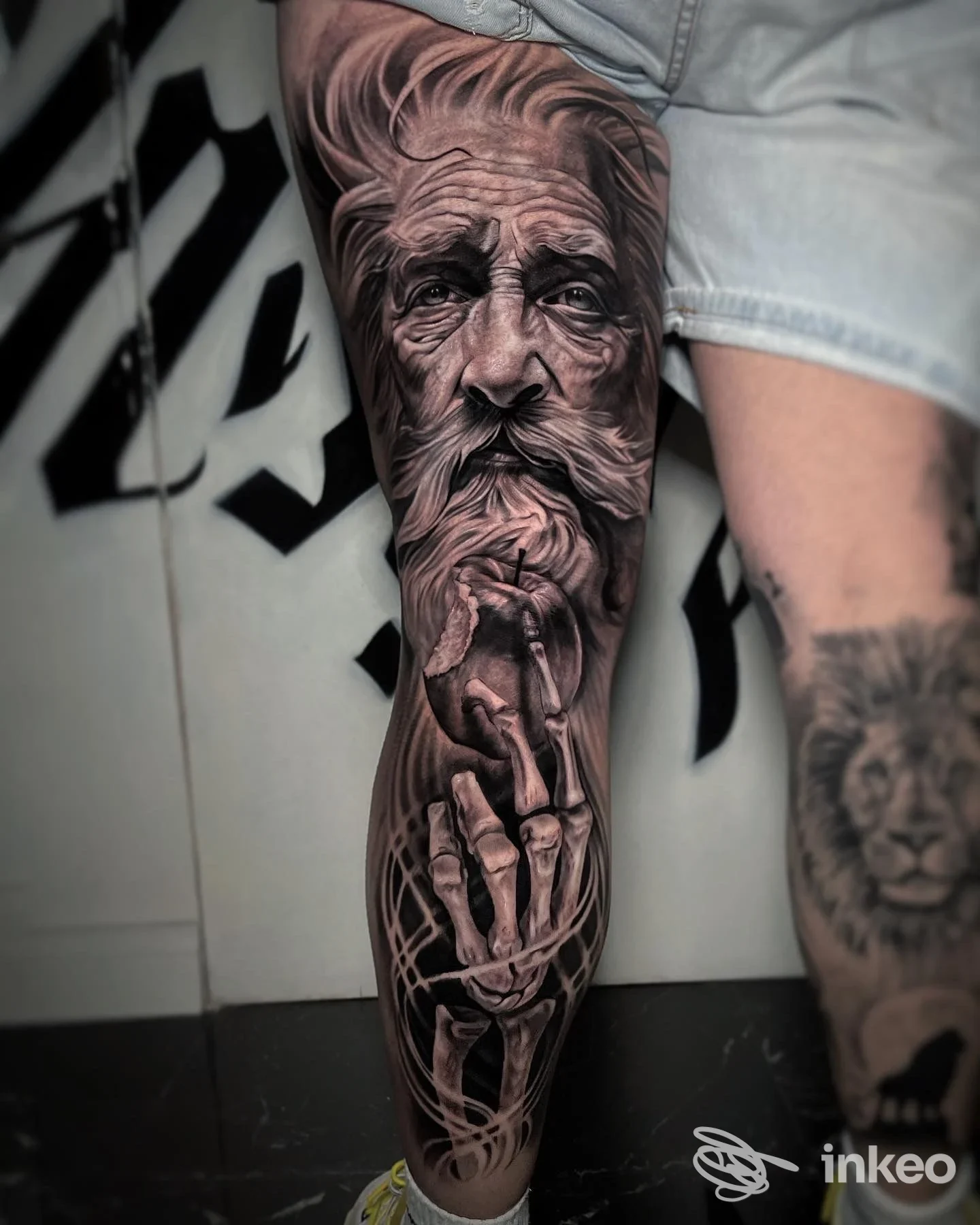 Tattoo realistico sul polpaccio raffigurante un vecchio uomo con barba, accompagnato da una mano scheletrica, realizzato sulla pelle.