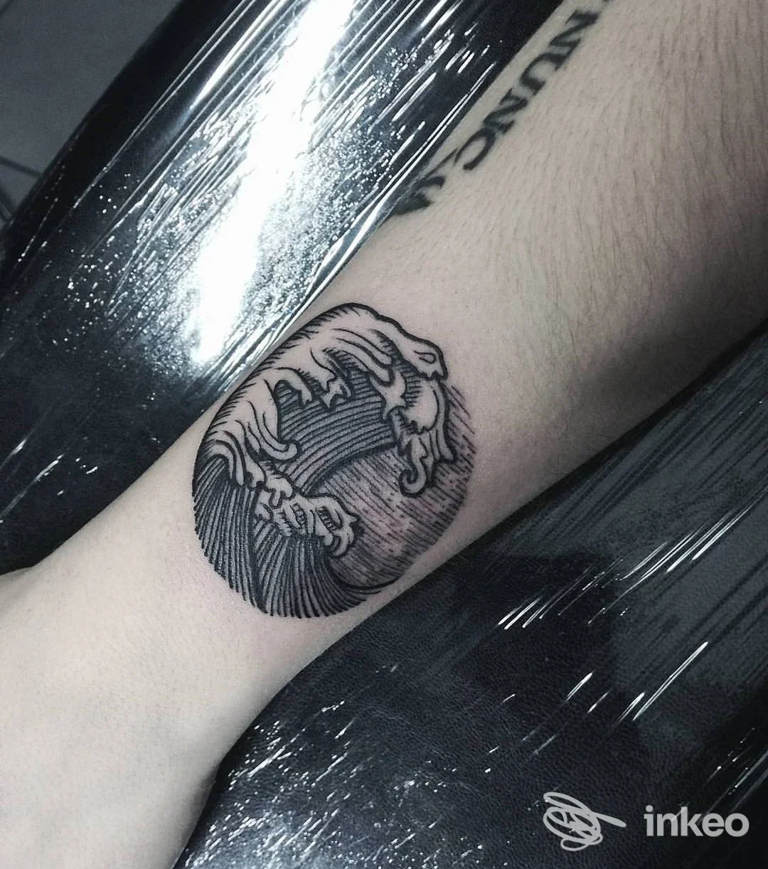 Tattoo circolare con onde stilizzate e una mano che sembra emergere, realizzato sulla parte interna del avambraccio di una persona, in bianco e nero.