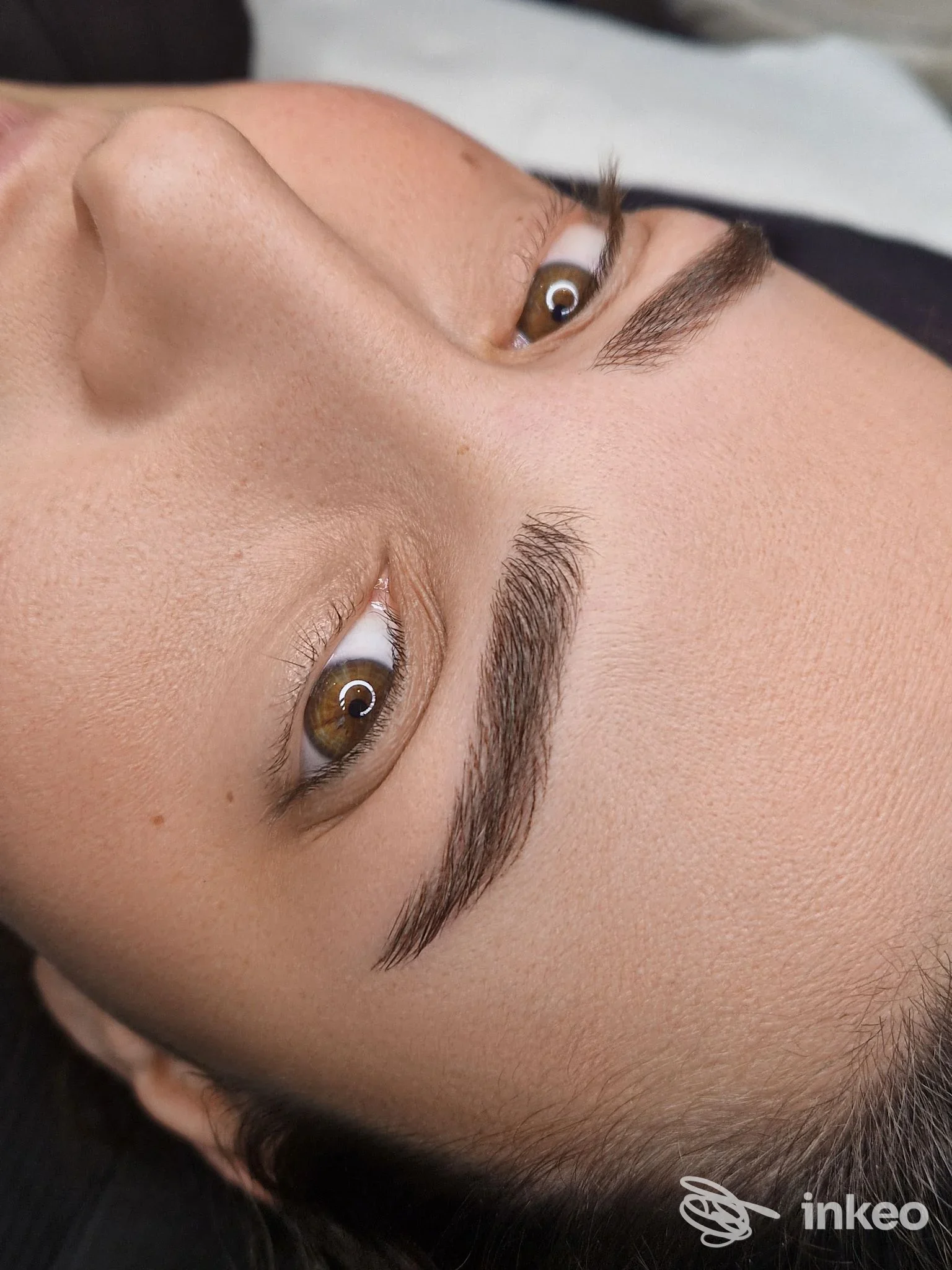 Primo piano di sopracciglia con trucco permanente ben definito applicato sulla pelle, viso parzialmente visibile.