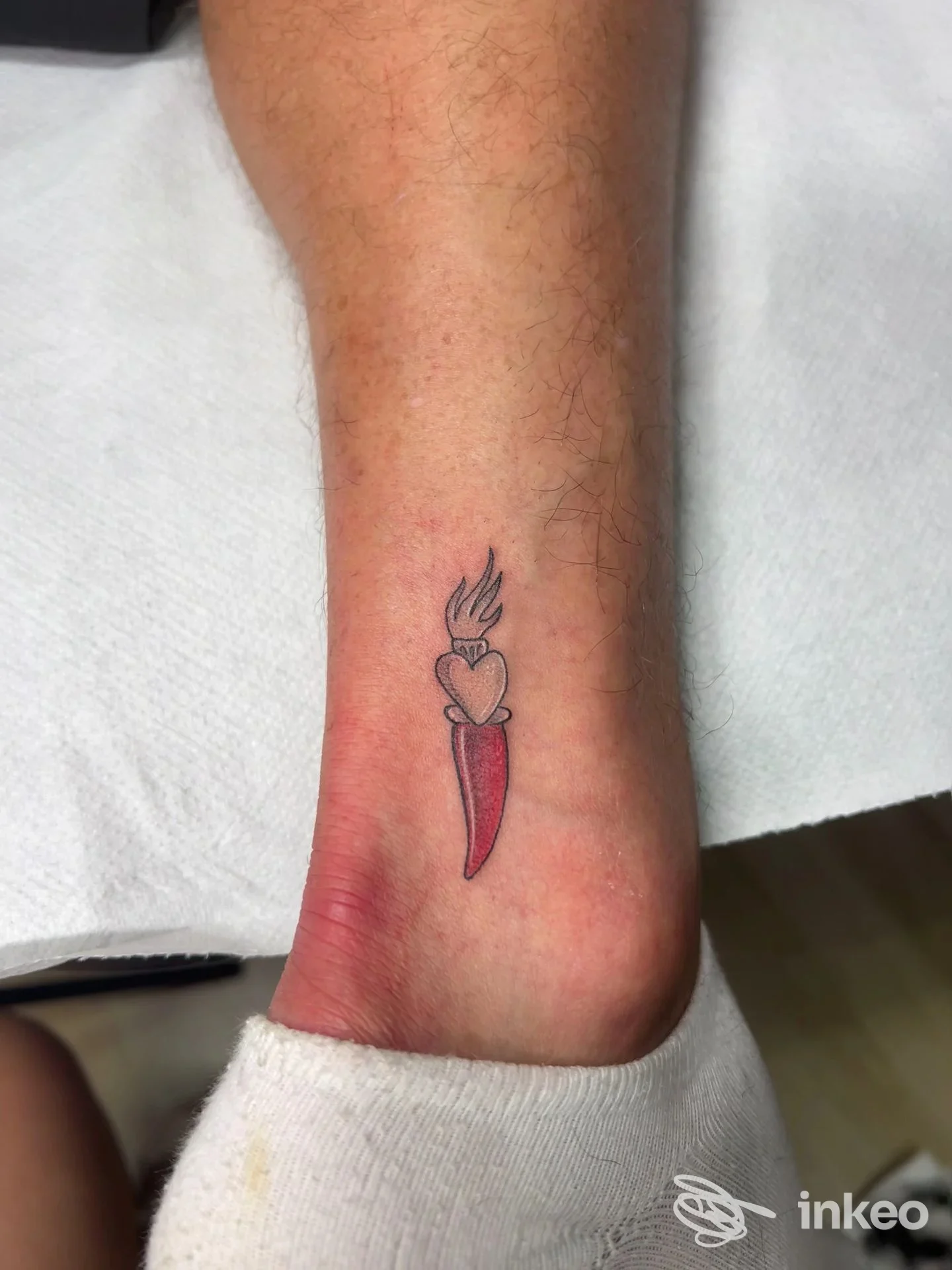 Tattoo sull'avambraccio/nelle vicinanze della caviglia: cuore con fiamma e spada rossa, colore intenso e linee nette.