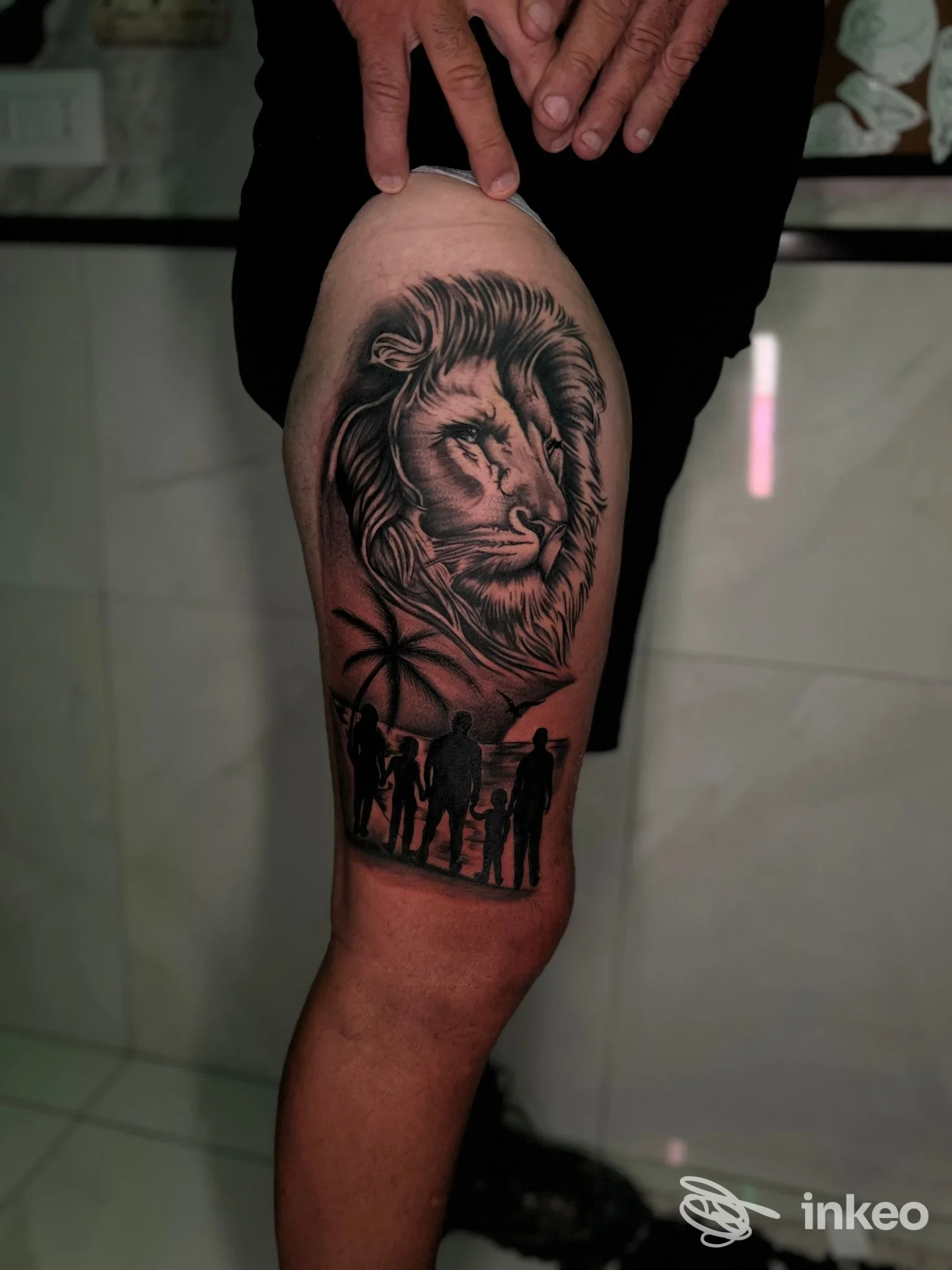Parte inferiore della gamba con tatuaggio realistico di un leone e silhouette di persone sullo sfondo; mani che sostengono la gamba, sfondo chiaro e riflessi.