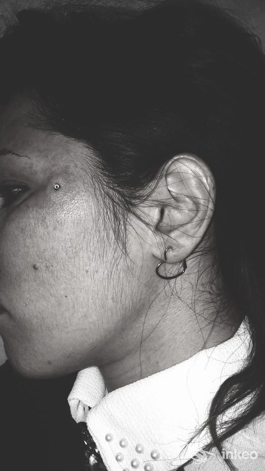 Particolare ritratto laterale di una persona, viso visibile solo parzialmente, che mostra un piercing all'orecchio e un piccolo piercing sulla tempia.