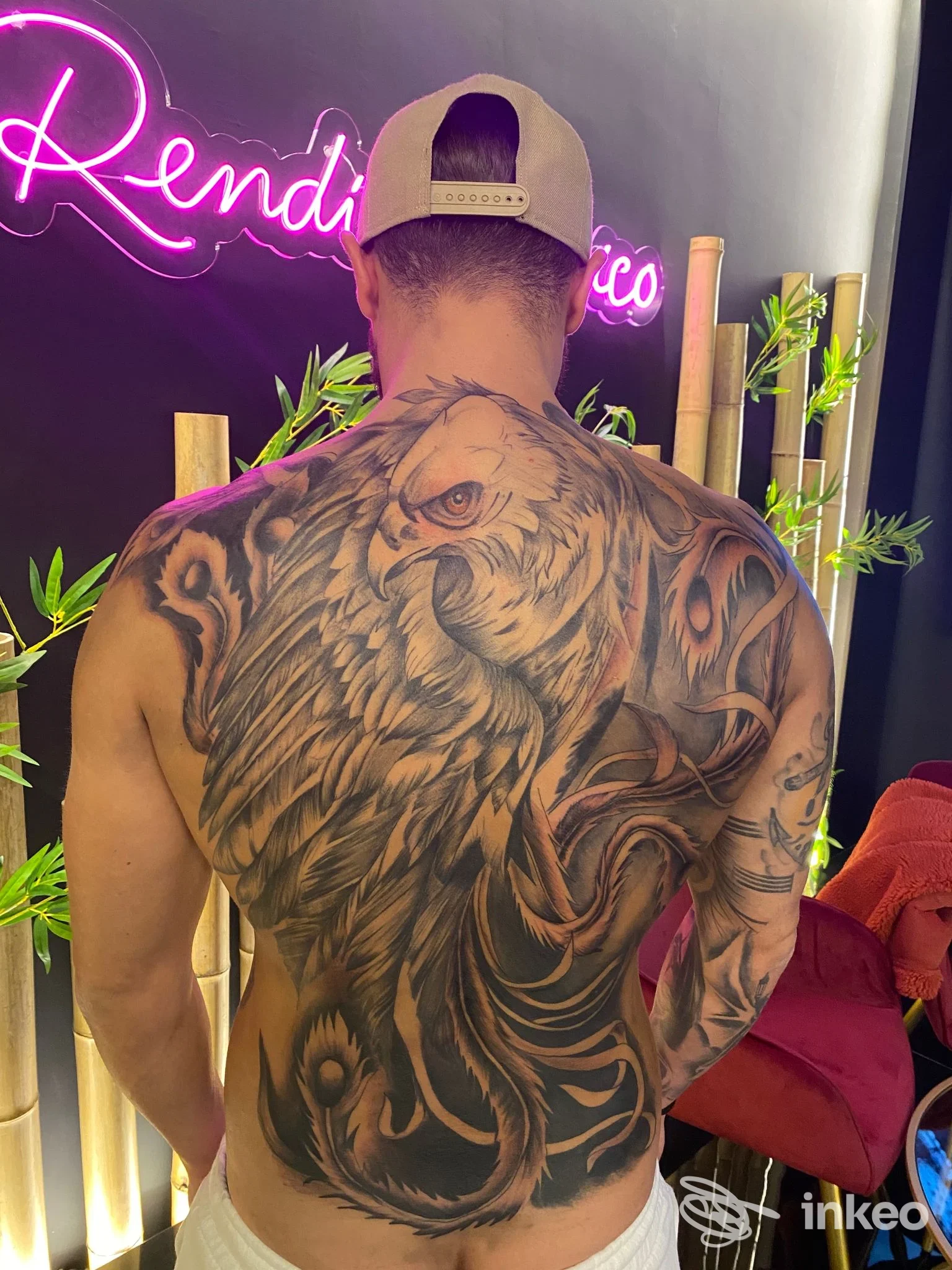 Tatuaggio molto grande sulla schiena di un uomo visto da dietro, con disegno realistico di animale; studio Amon Ra Tattoo a Calvizzano, atmosfera con sfondo neon e arredi.